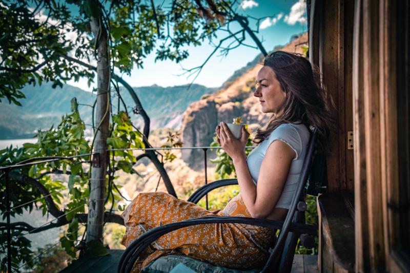 Frau, die auf einem Schaukelstuhl Tee trinkt, Terrasse mit Blick auf den See