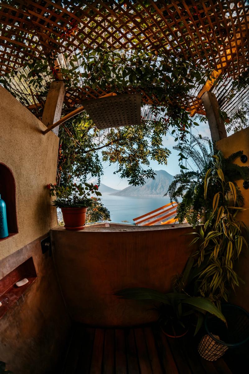 Kupferbadewanne im Freien, umgeben von Pflanzen, mit Panoramablick auf Vulkane und den See