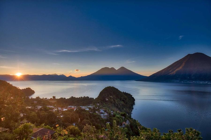 Sunrise over Lake Atitlan and its volcanoes, with village rooftops below