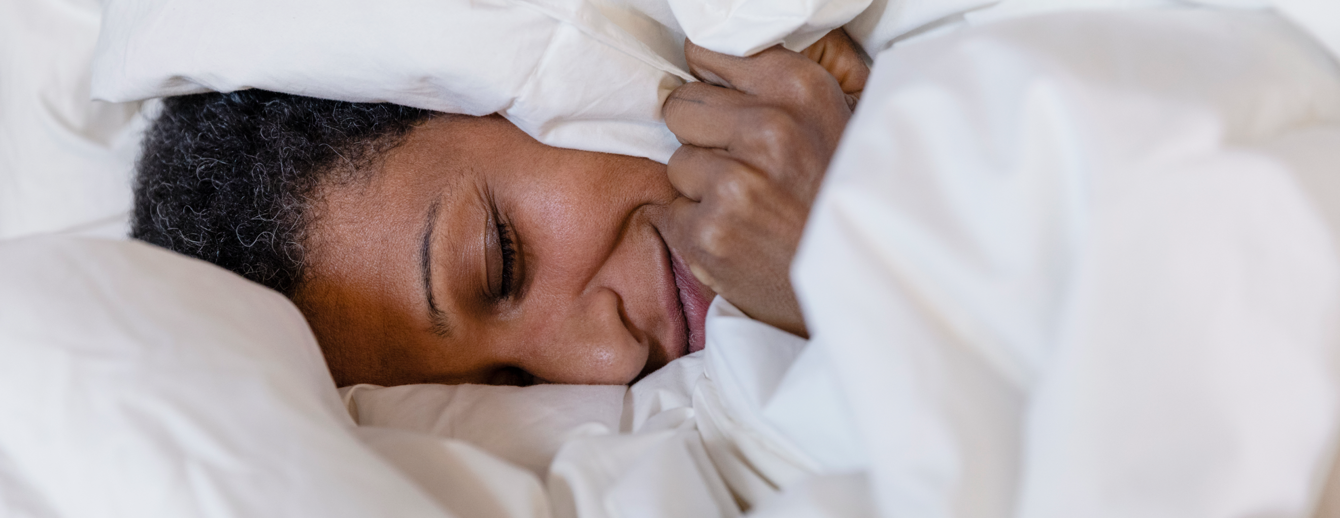A person laying in a cozy bed, covered in sheets