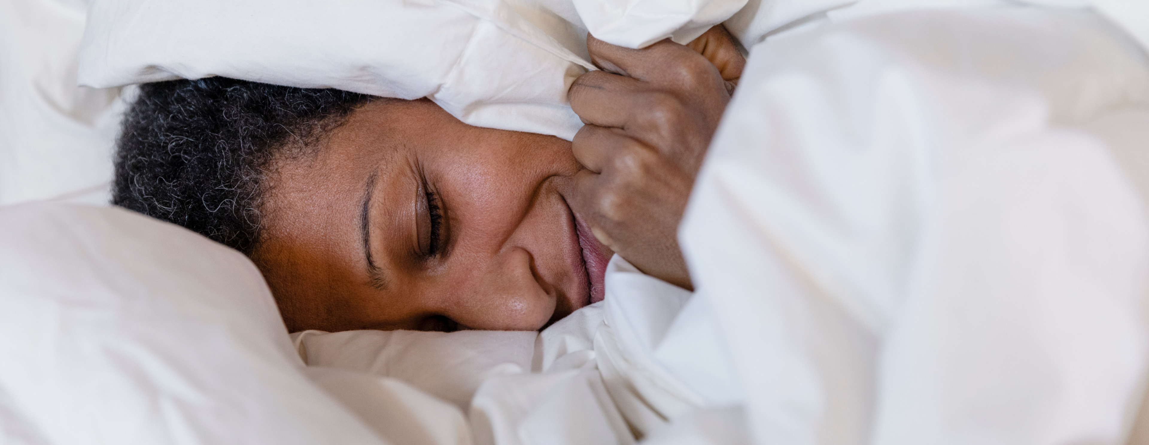 A person laying in a cozy bed, covered in sheets
