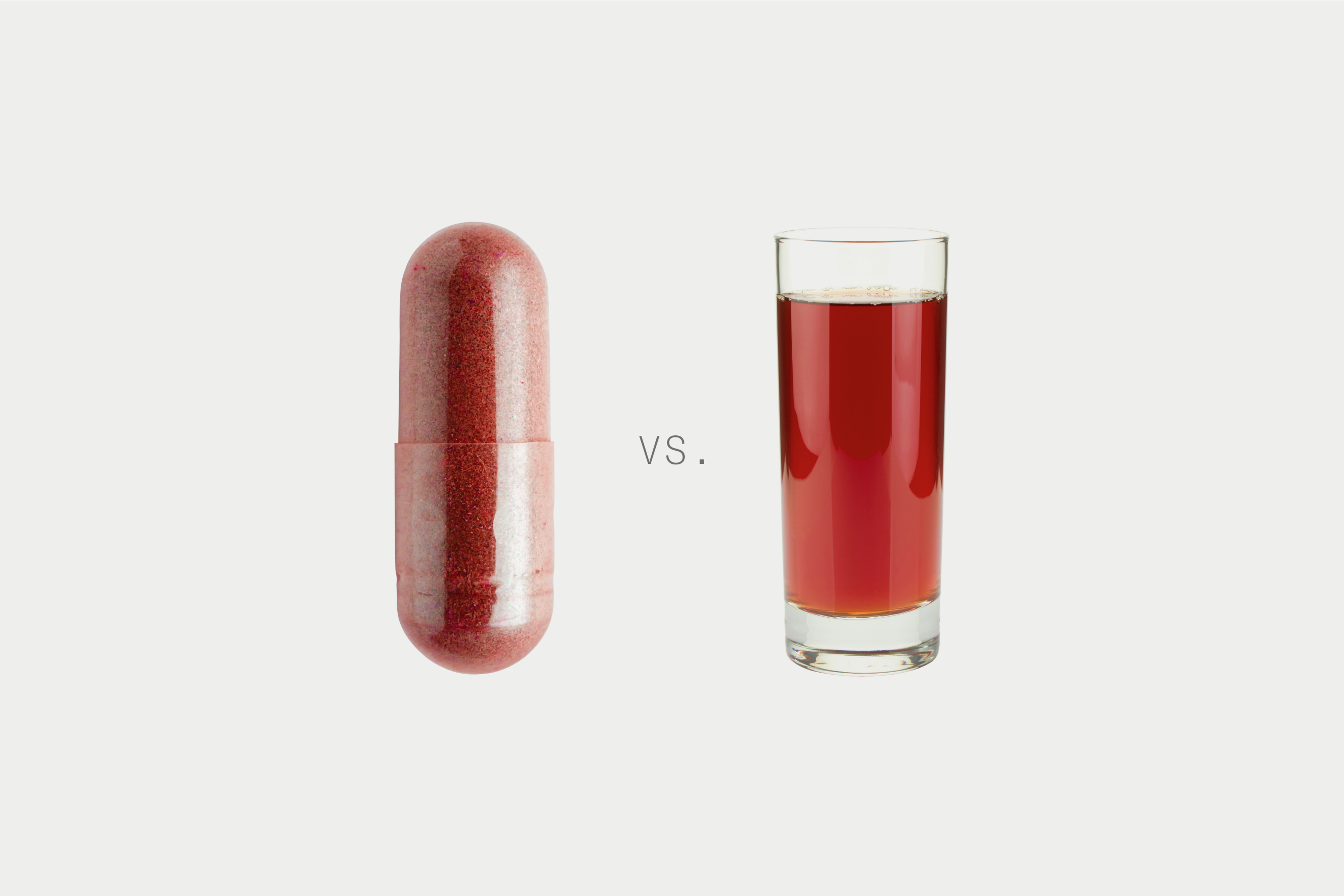 A pill capsule of pomegranate next to a cup of pomegranate juice