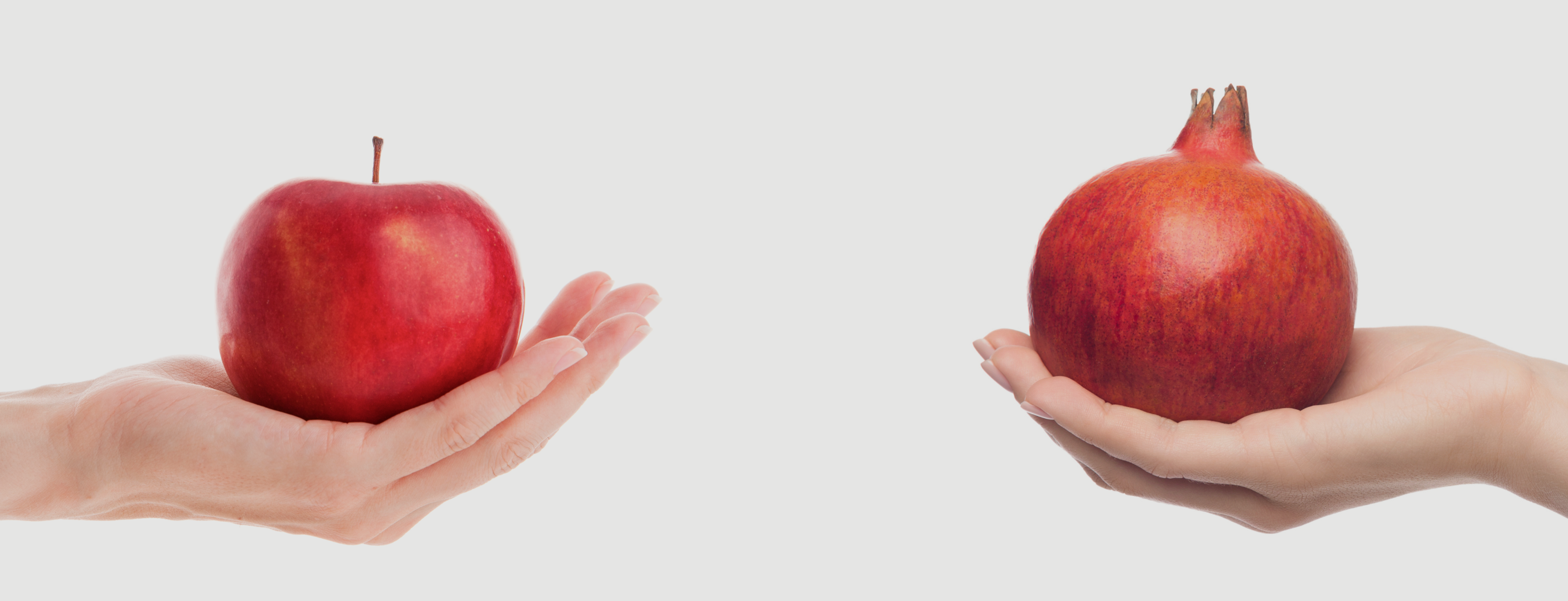 One hand on the left holding an apple, another hand on the right holding a pomegranate.