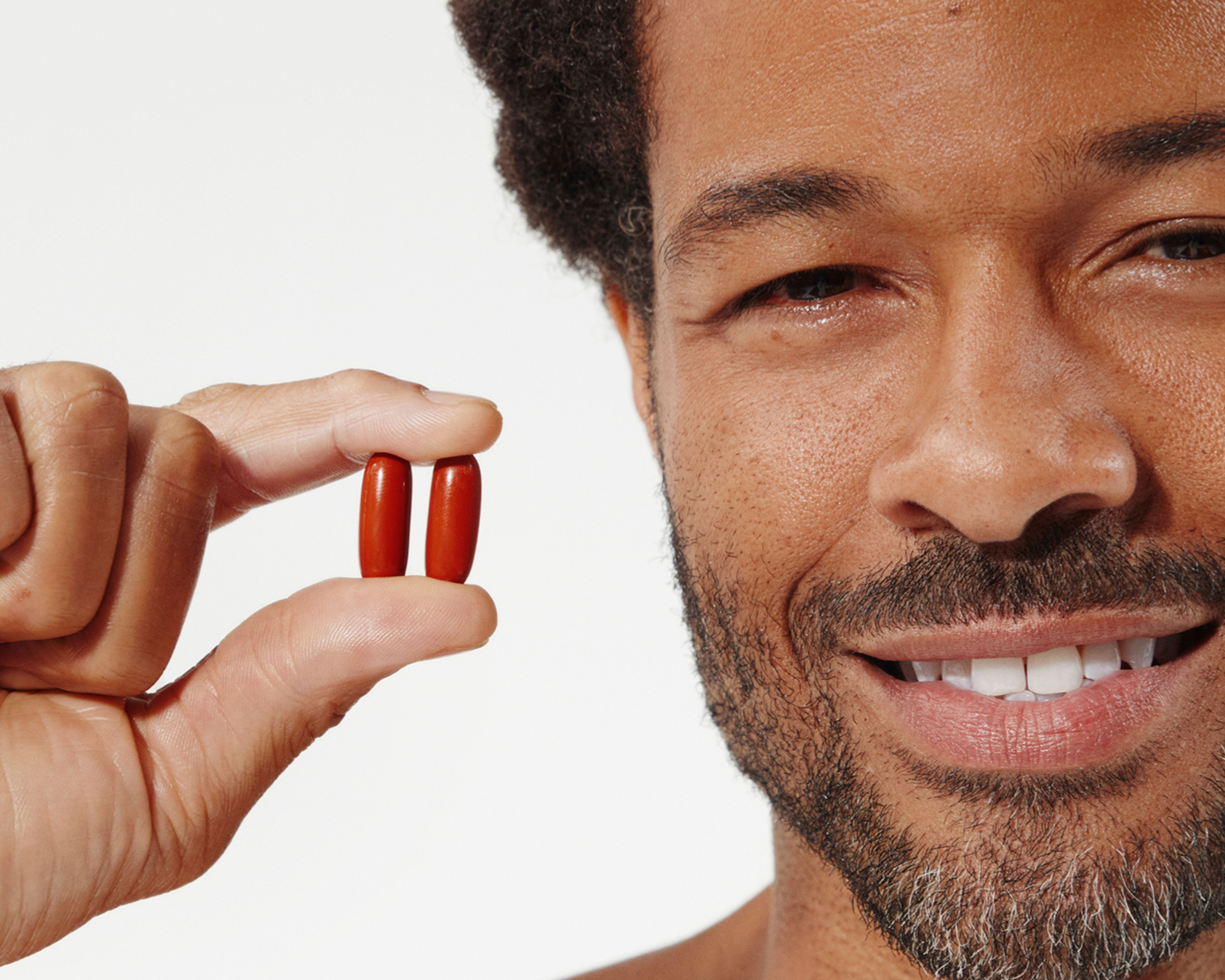 Smiling man holding two mitopure softgels that are red in color