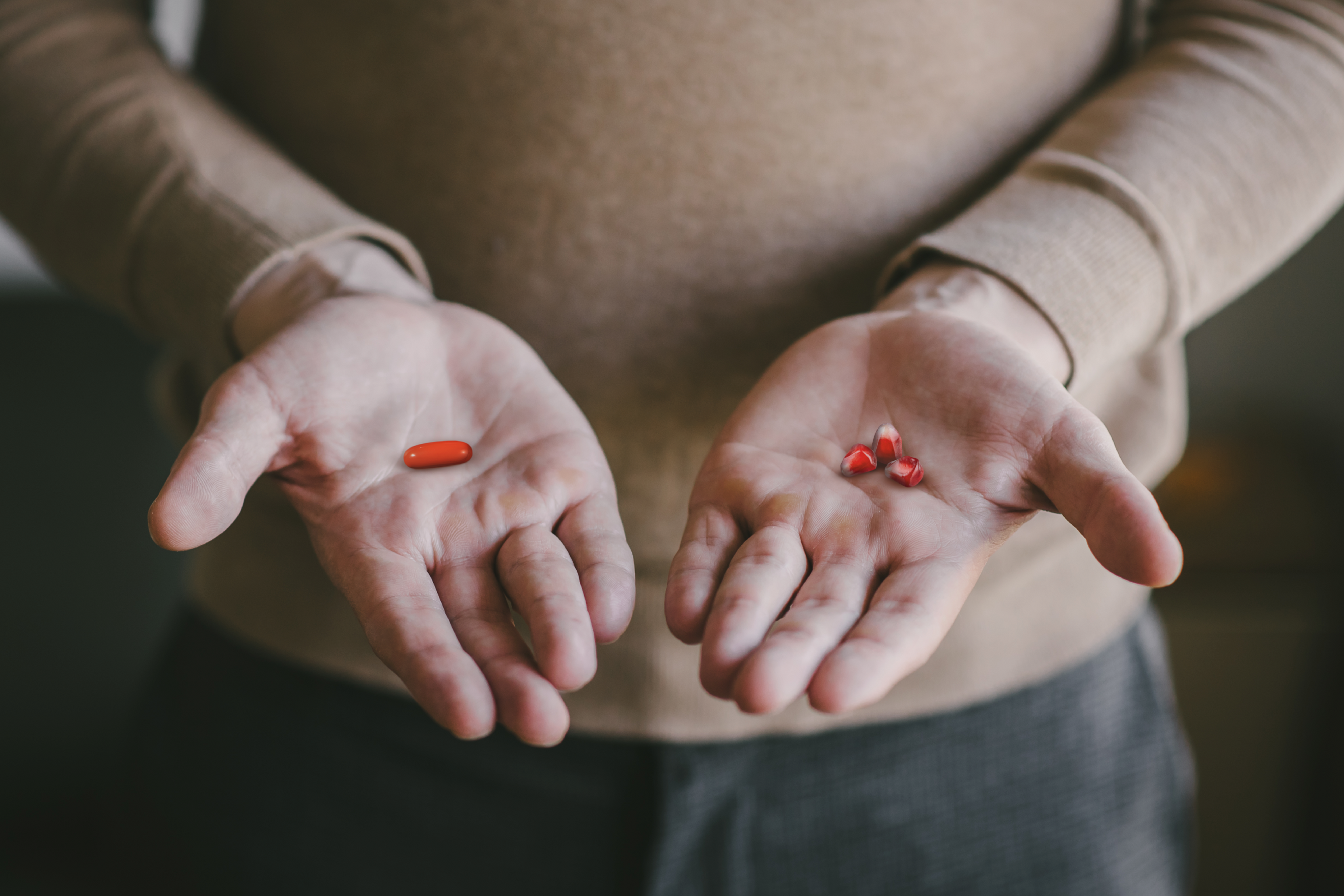 Person holding in one hand a Mitopure (Urolithin A) softgels and pomegranate kernel seeds in the other.