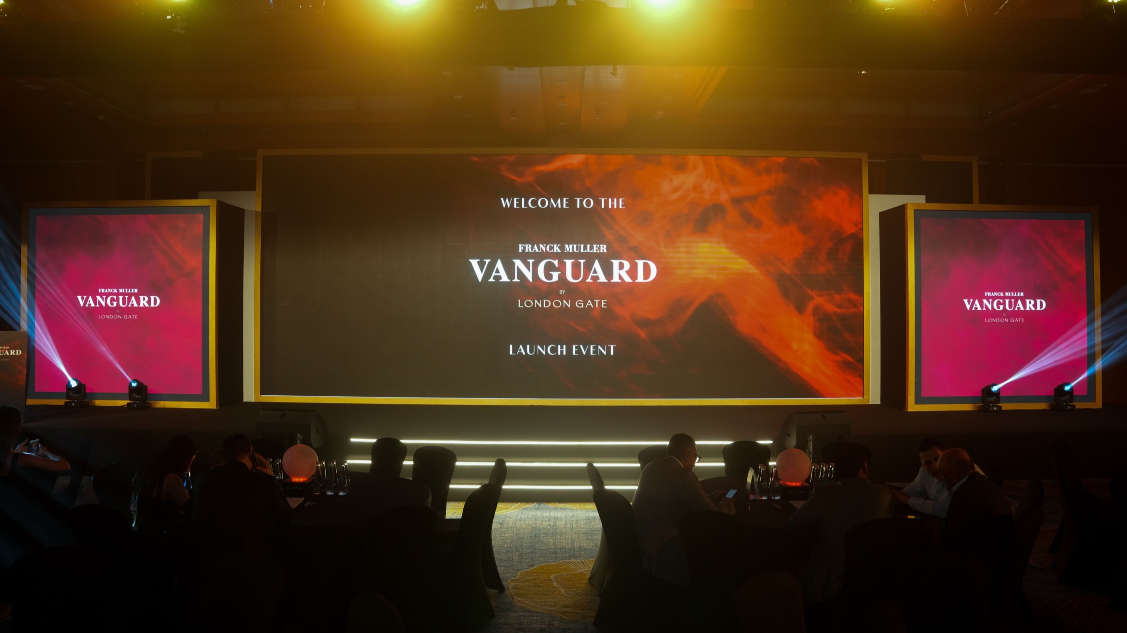 Audience seated in an event, screens displaying the event name and details