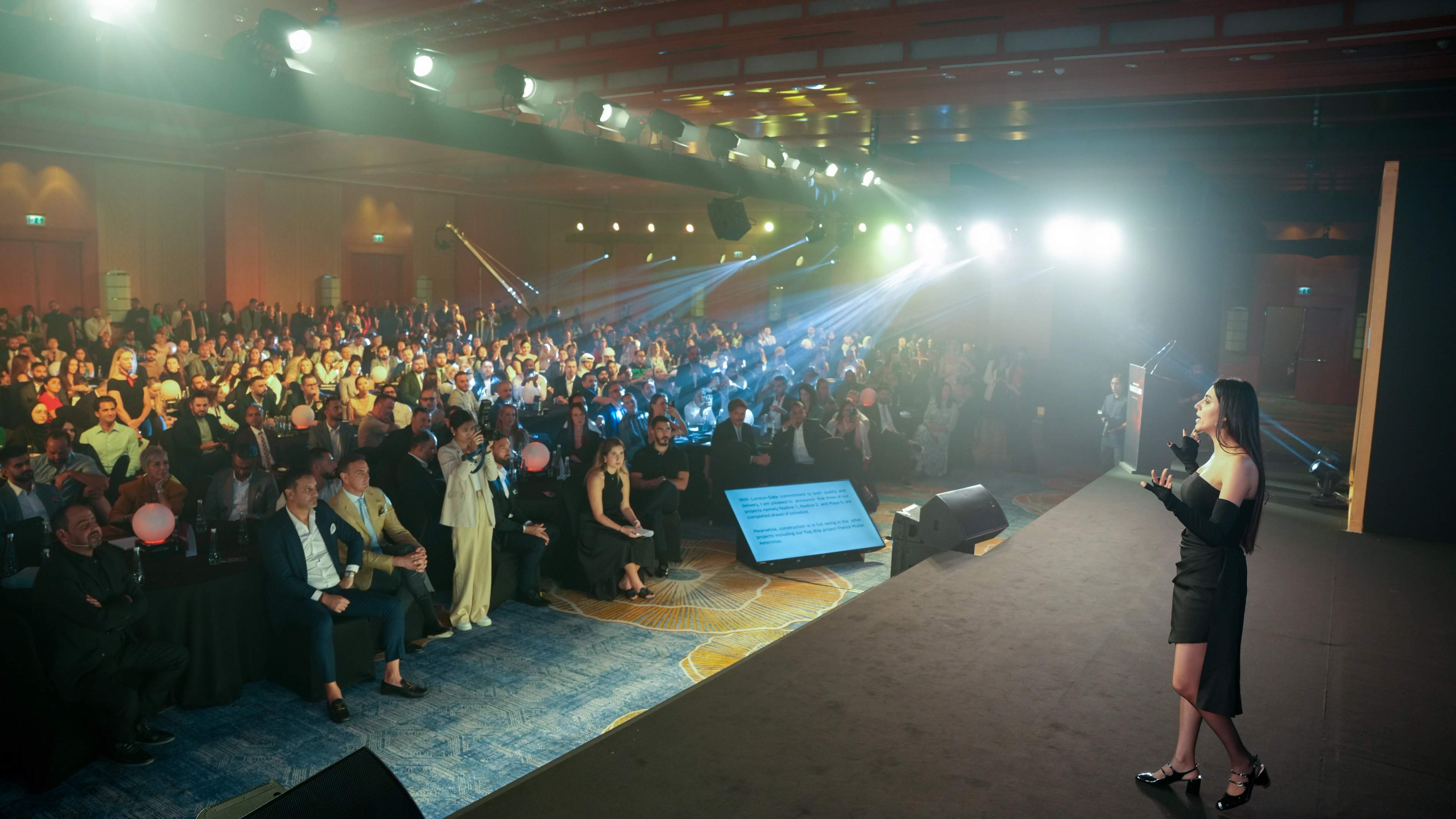 Presenter on stage addressing a full ballroom at a luxury launch