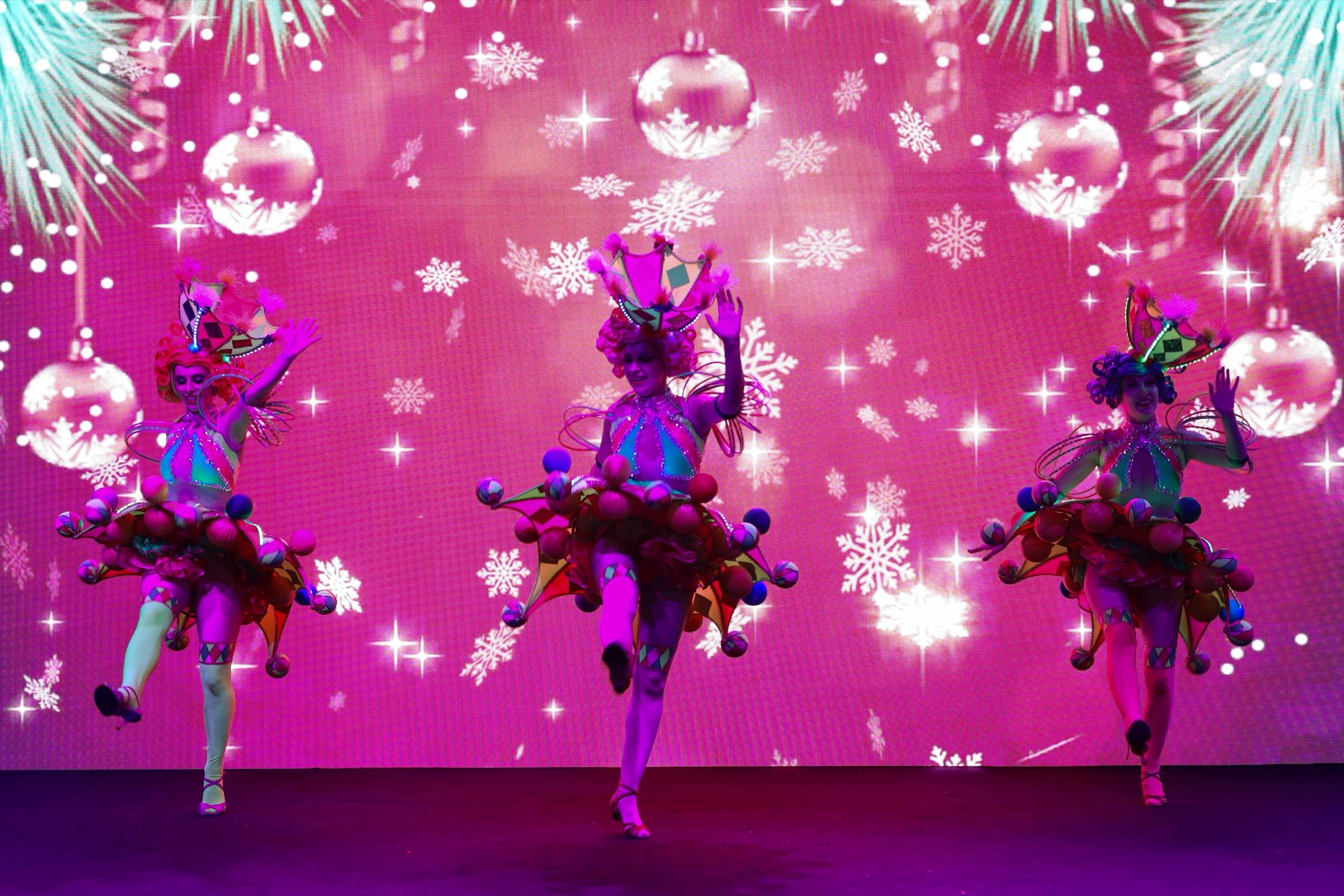 Costumed dancers performing on a pink-lit stage