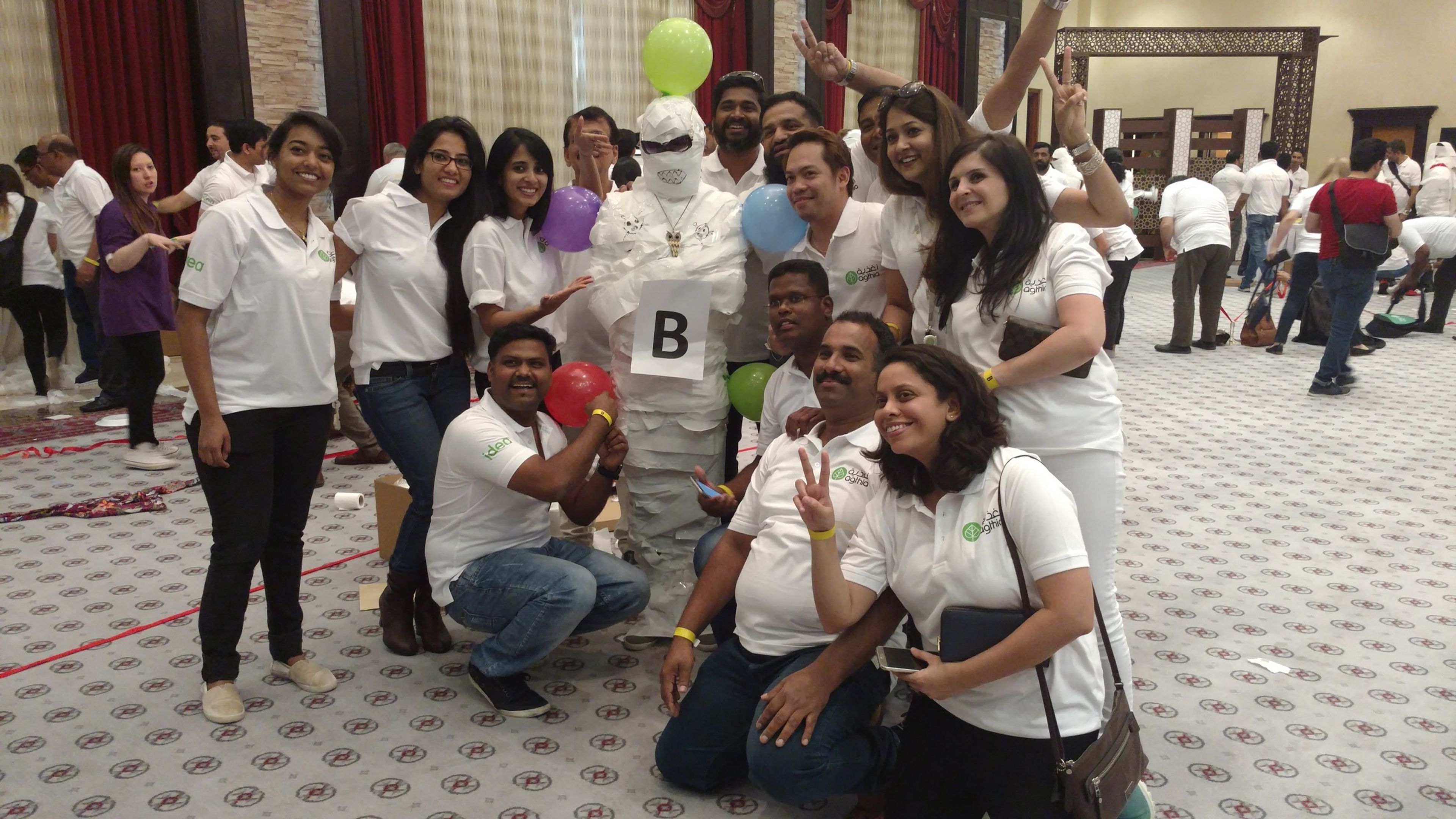 Colleagues in matching white T-shirts celebrating after a wrap-the-mummy challenge at an indoor team building event