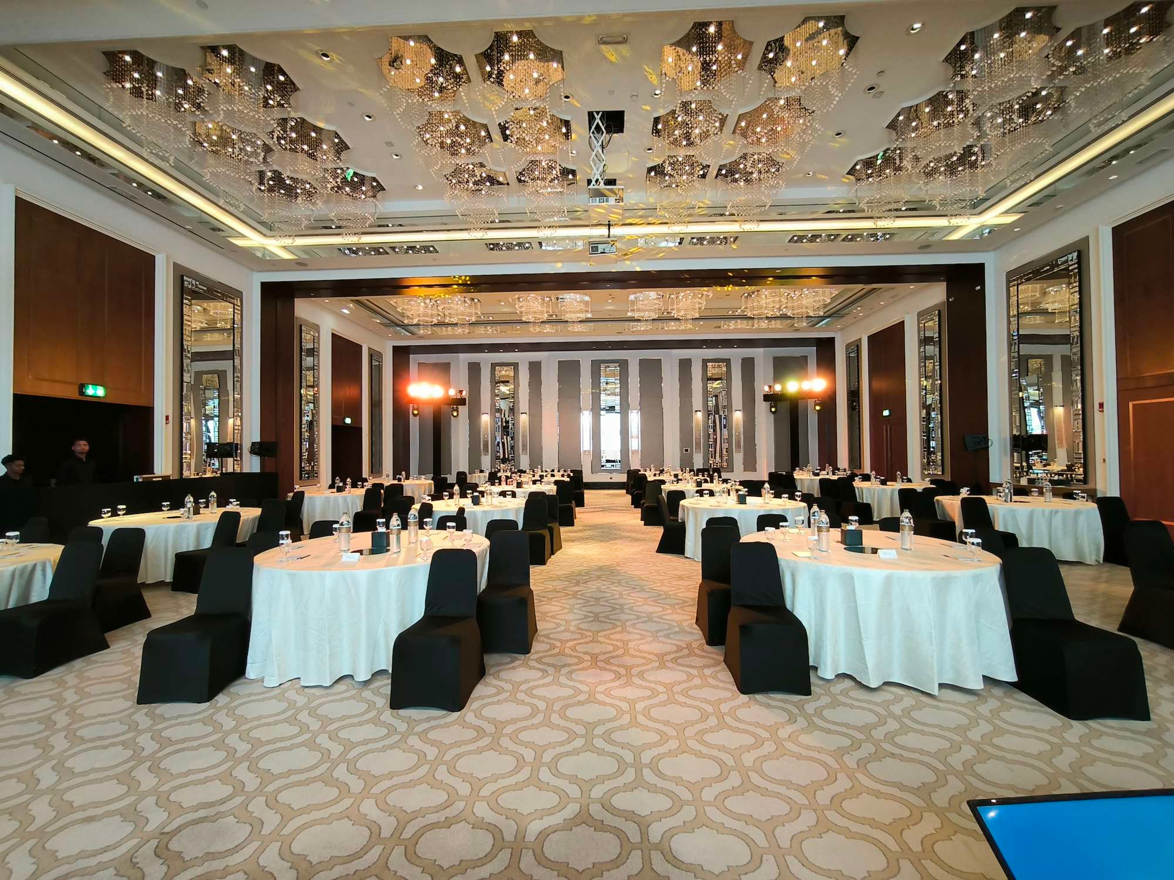 Corporate conference ballroom with round tables, black chair covers and stage lighting, set up for a conference