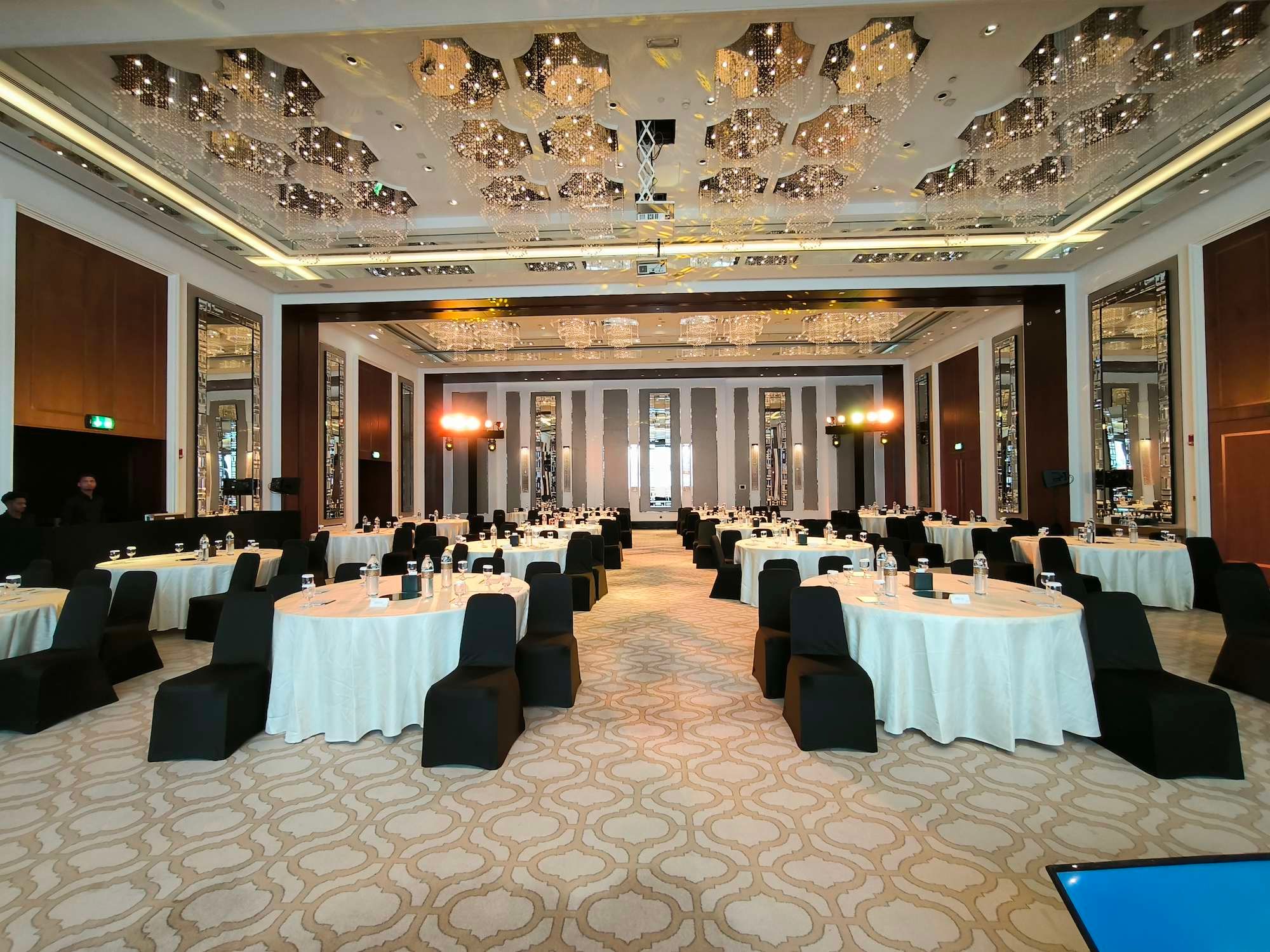 Corporate conference ballroom with round tables, black chair covers and stage lighting, set up for a conference