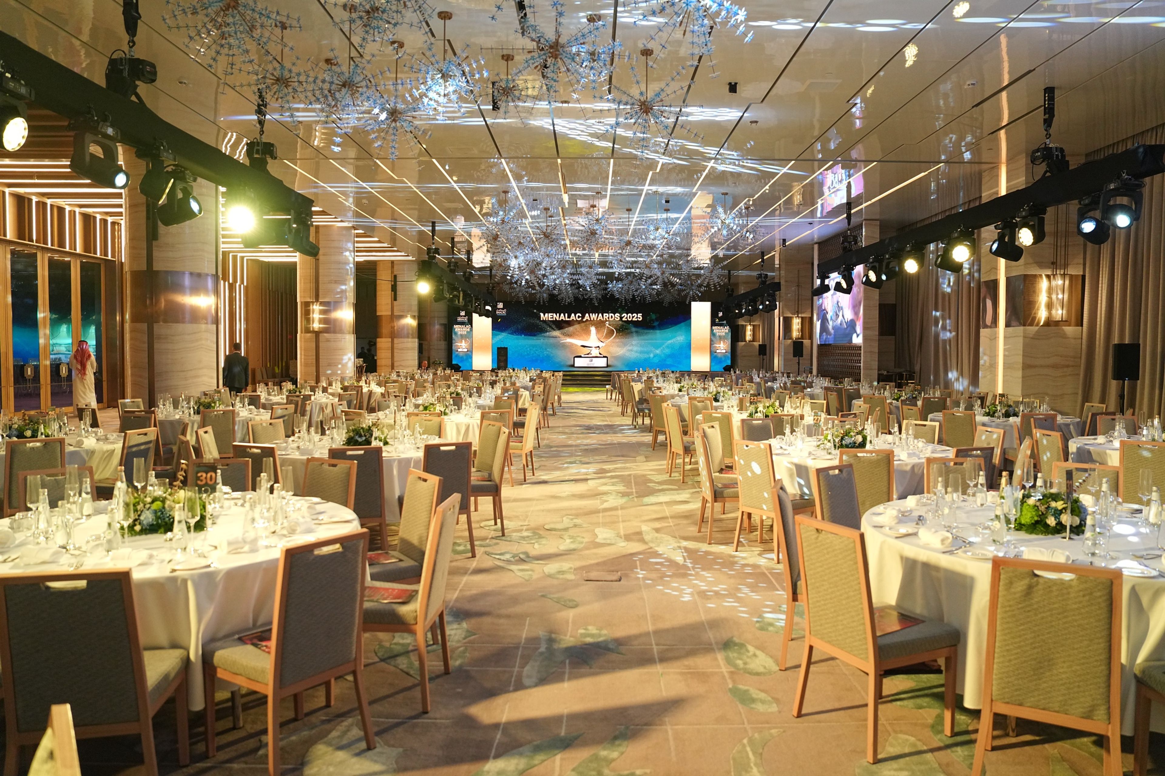 Hotel ballroom set for a corporate gala dinner with round tables, crystal ceiling and a stage screen