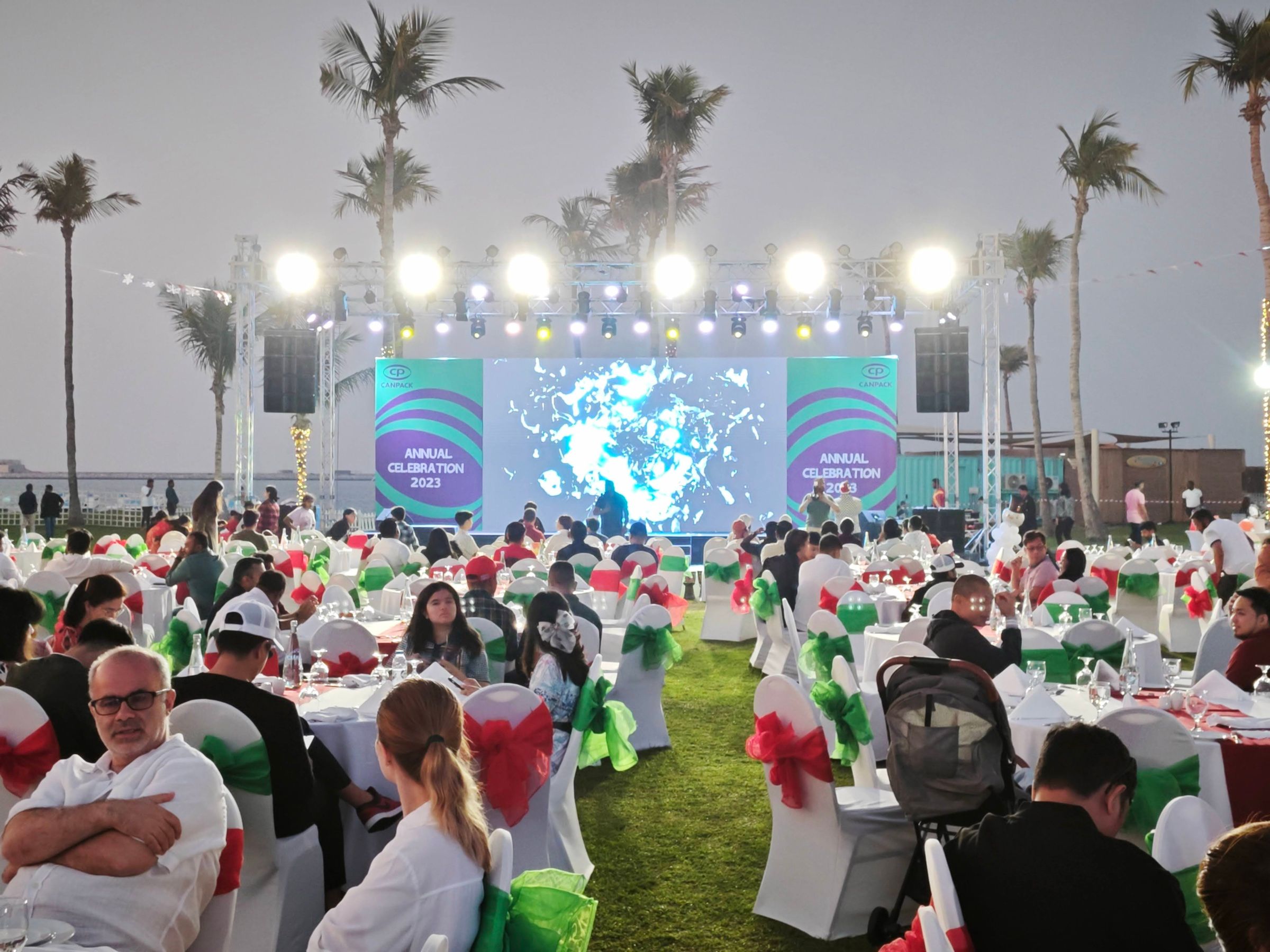 Outdoor corporate event with stage, lighting, and large digital screens