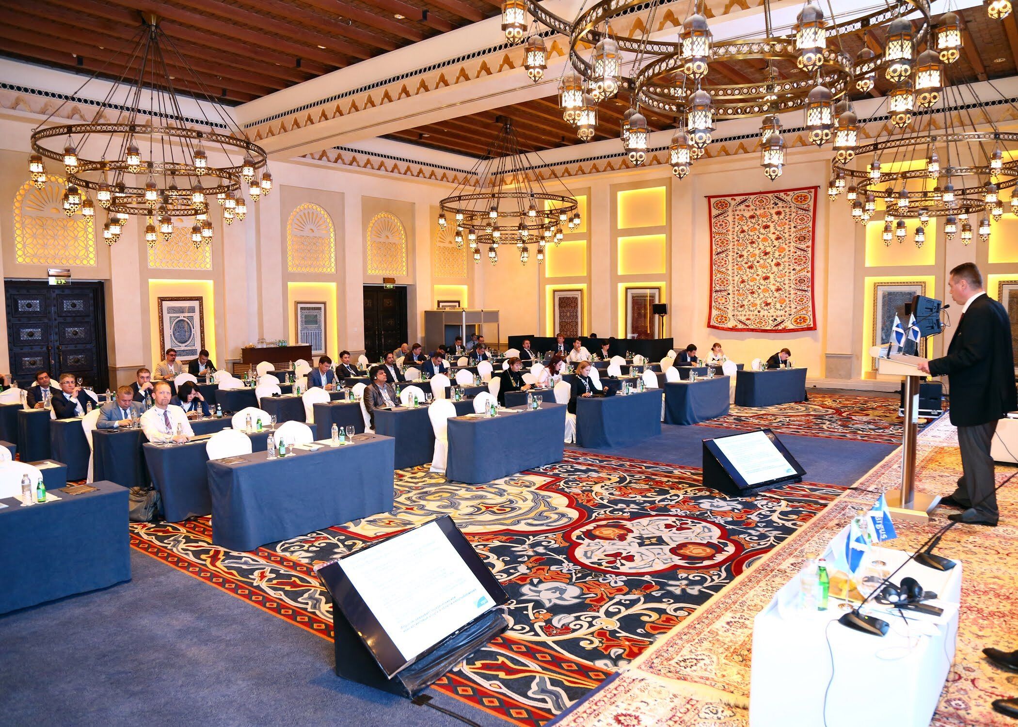 Delegates at a conference in an ornate ballroom with classroom-style seating