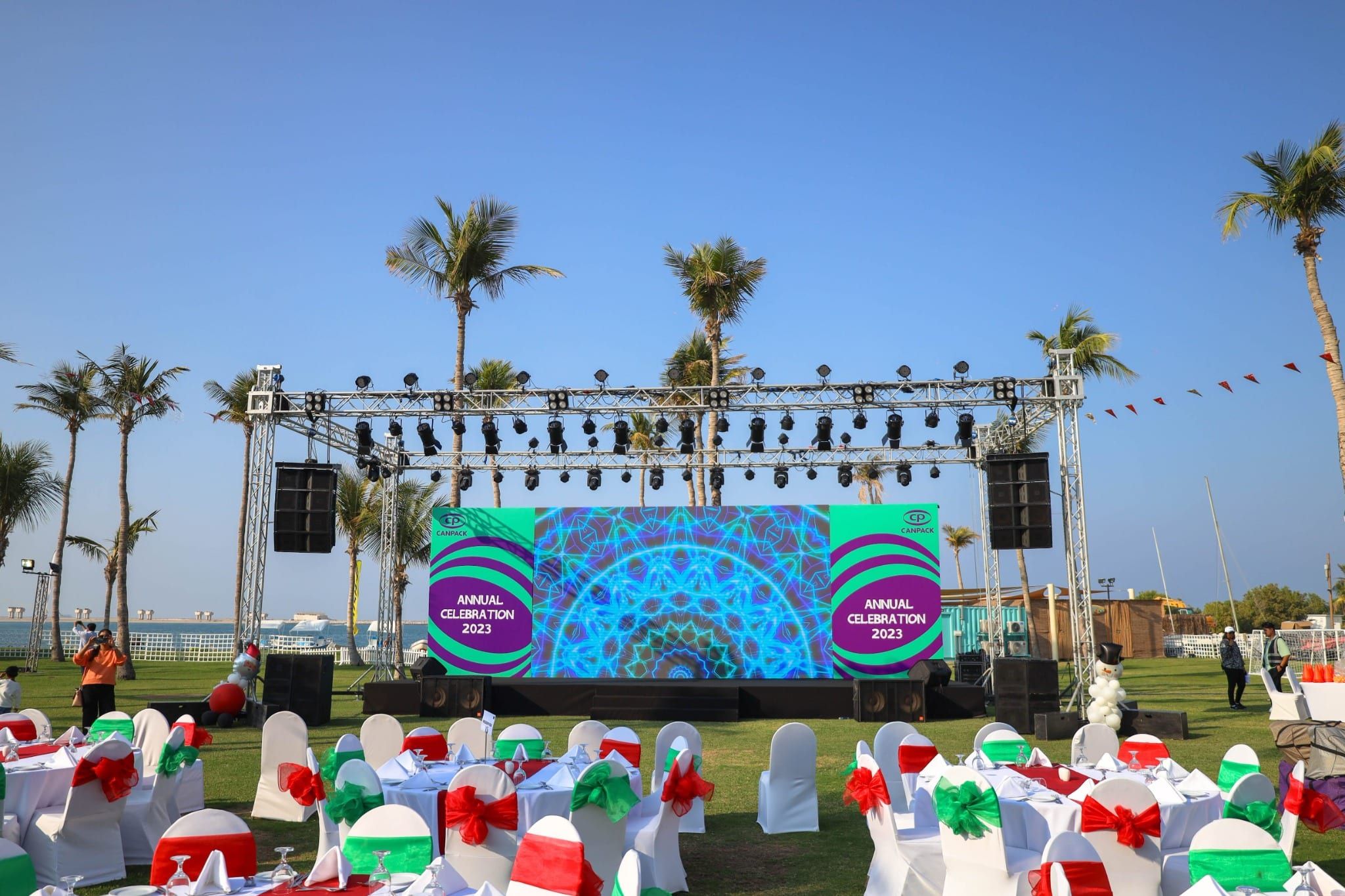 Outdoor stage with LED screen and truss lighting above tables dressed in red and green