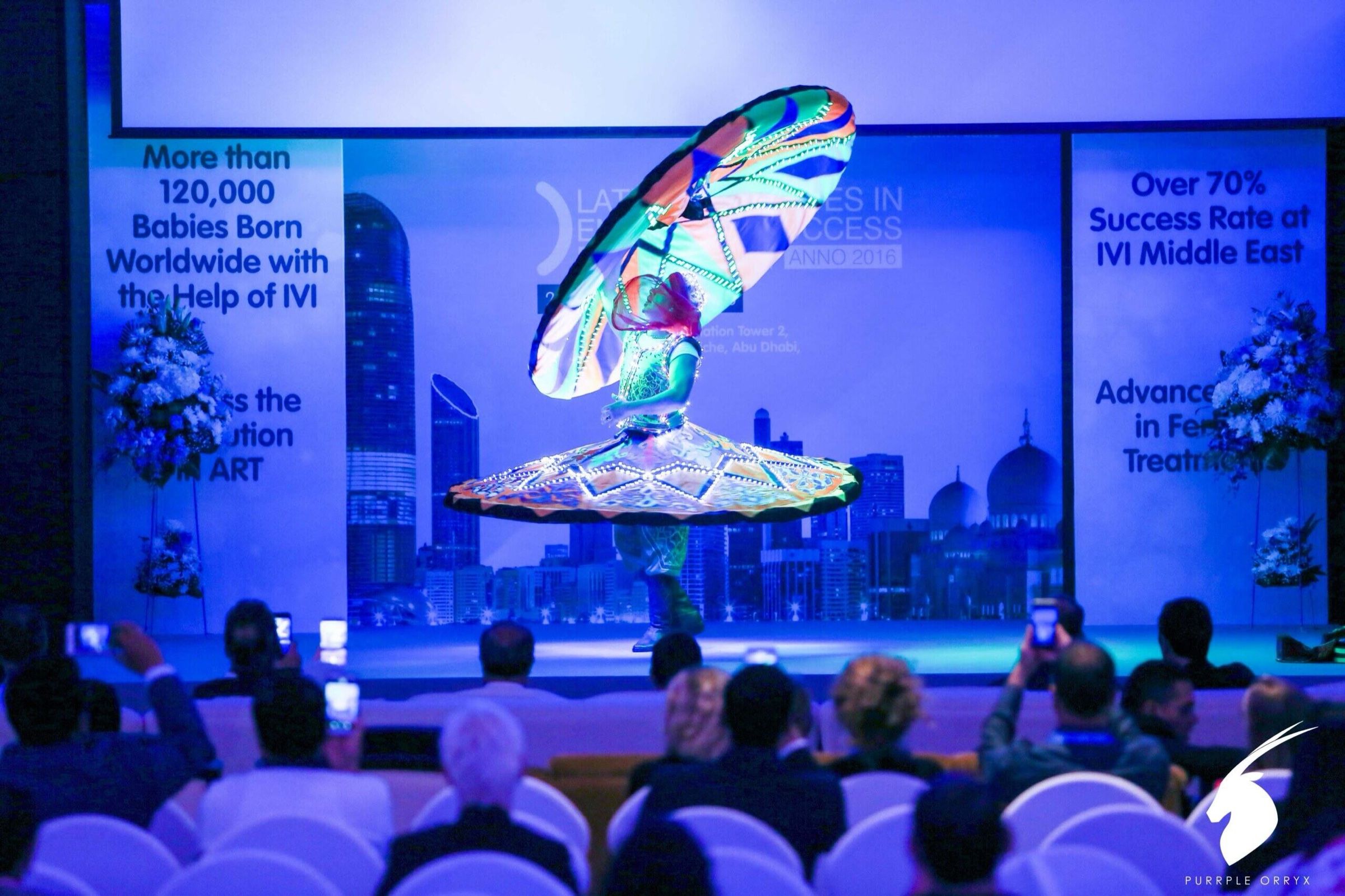 Speaker on stage with a large blue LED screen at a technology conference