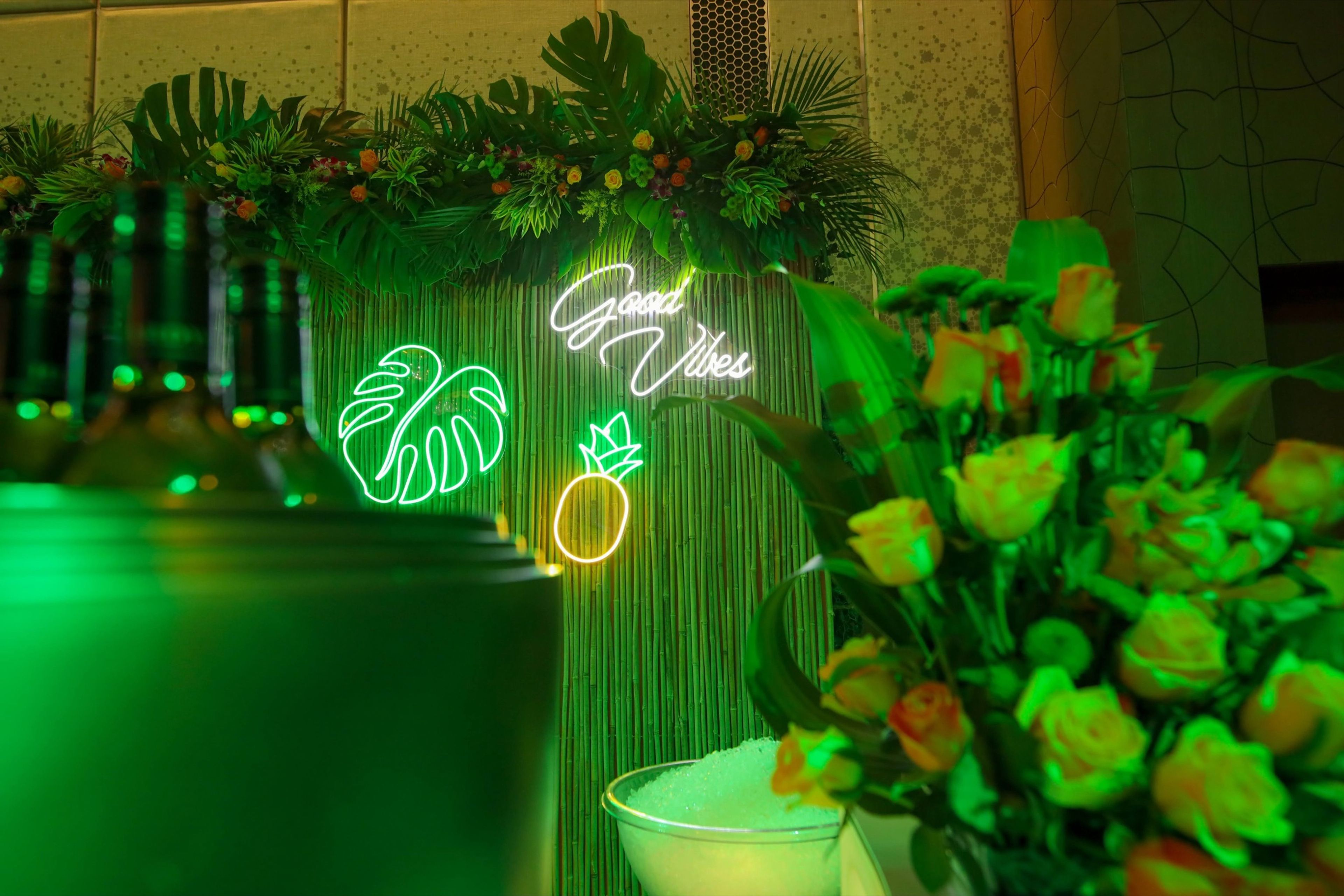 Green-lit tropical floral décor with a neon sign at a themed event