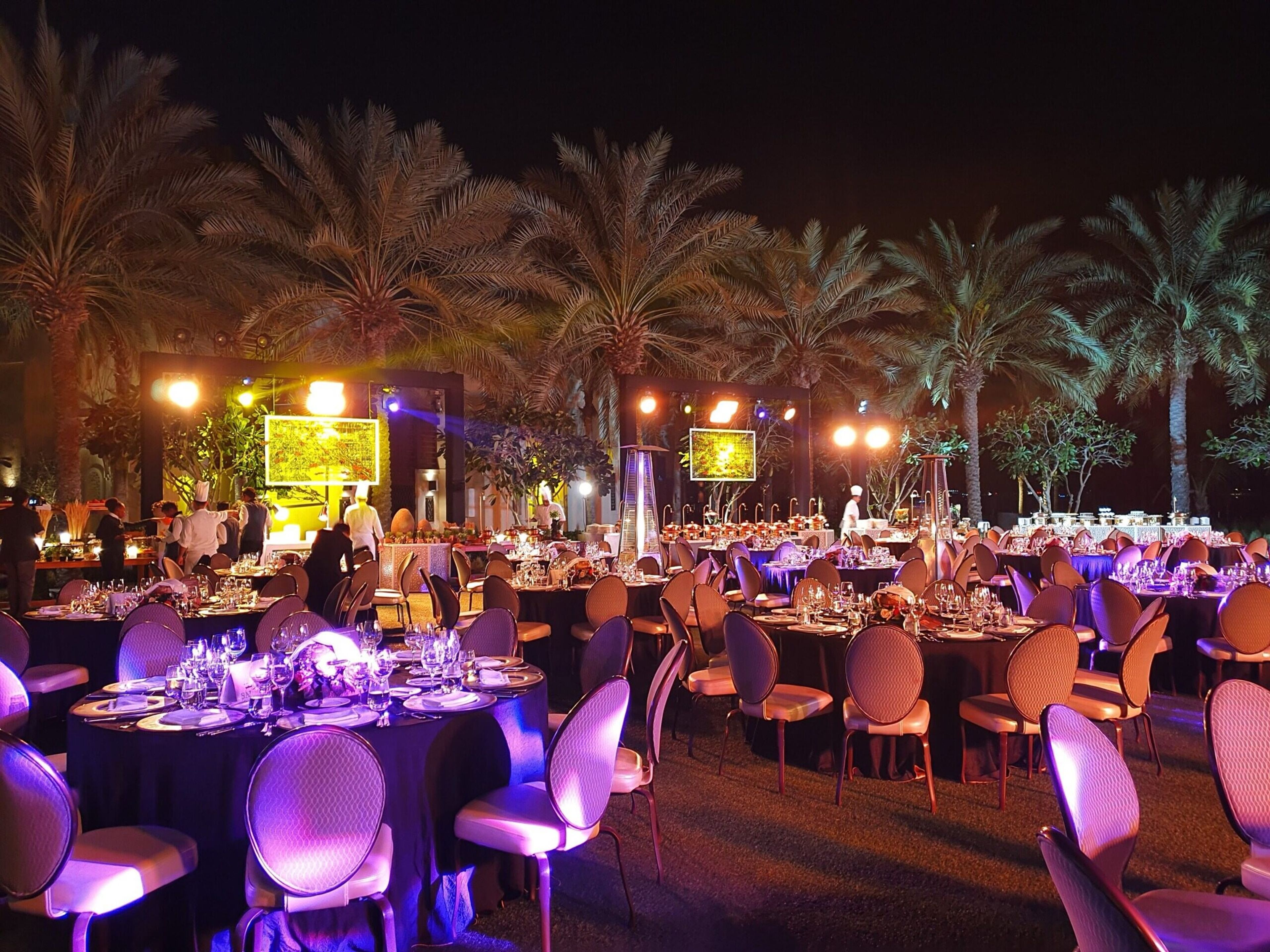 Outdoor gala dinner at night with purple lighting and palm trees