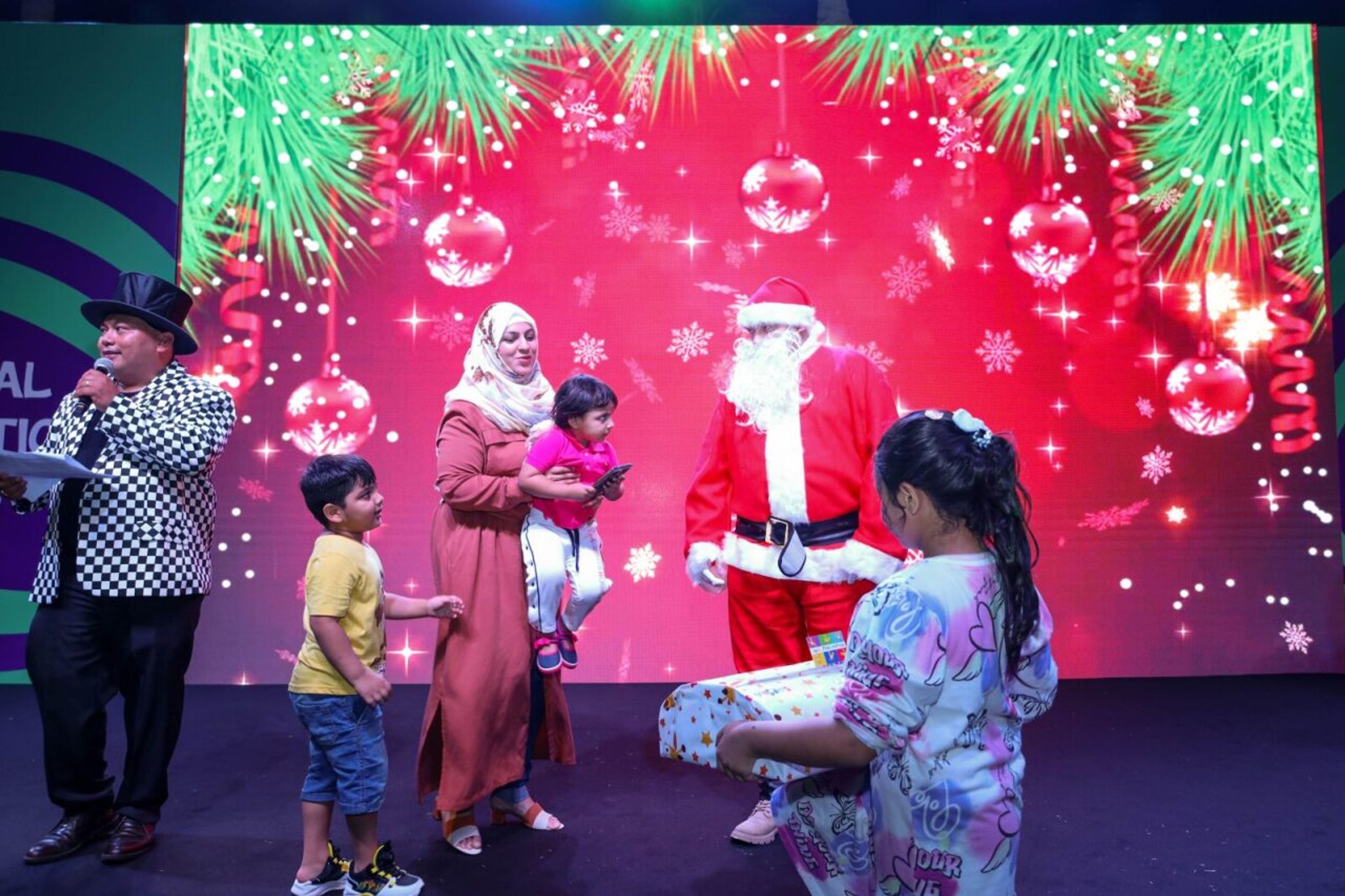 Santa handing out gifts to children on stage, with an MC, at a corporate Christmas family day in Dubai