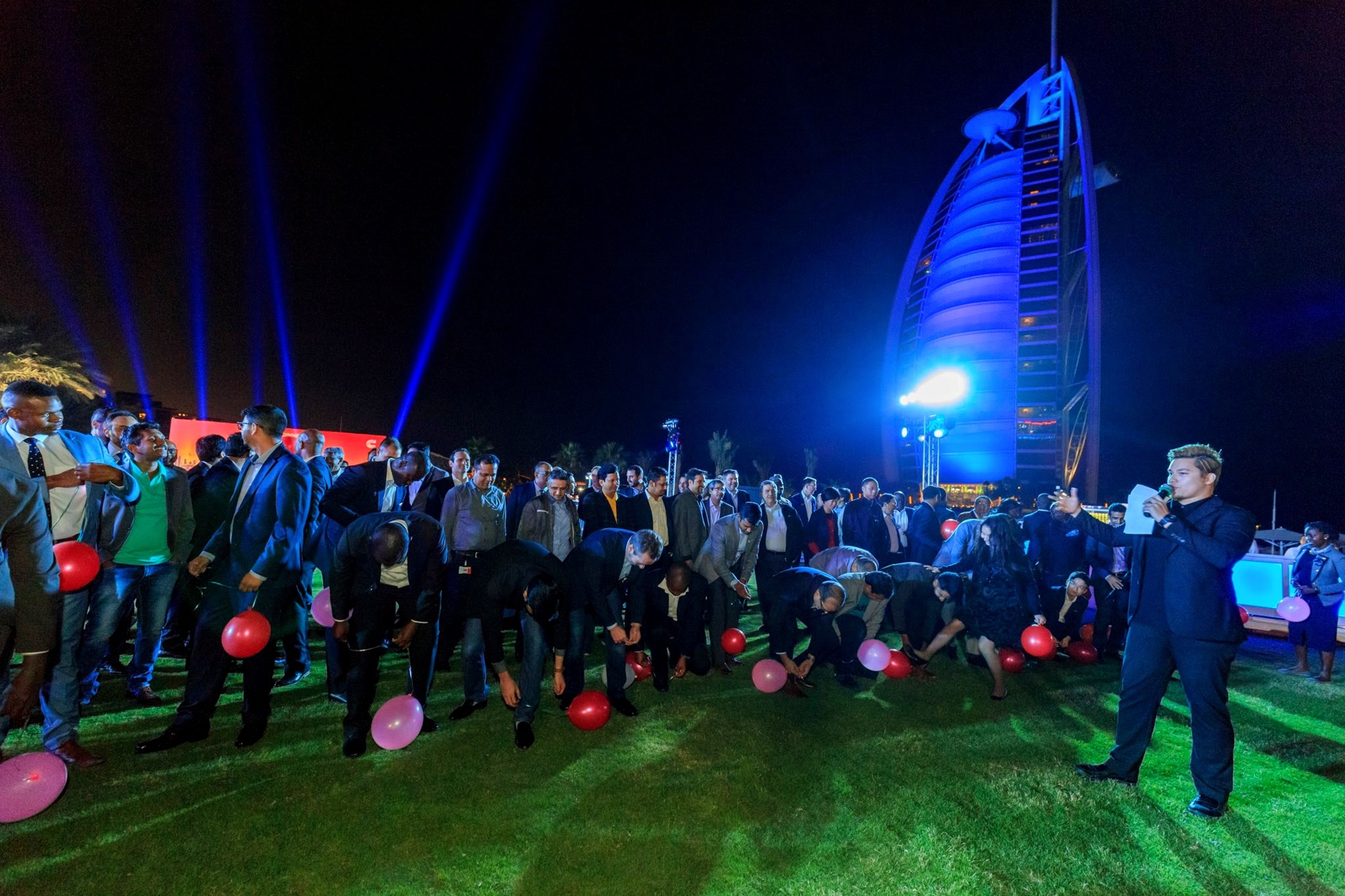 Large corporate group playing an outdoor balloon game at night, with the Burj Al Arab lit up behind