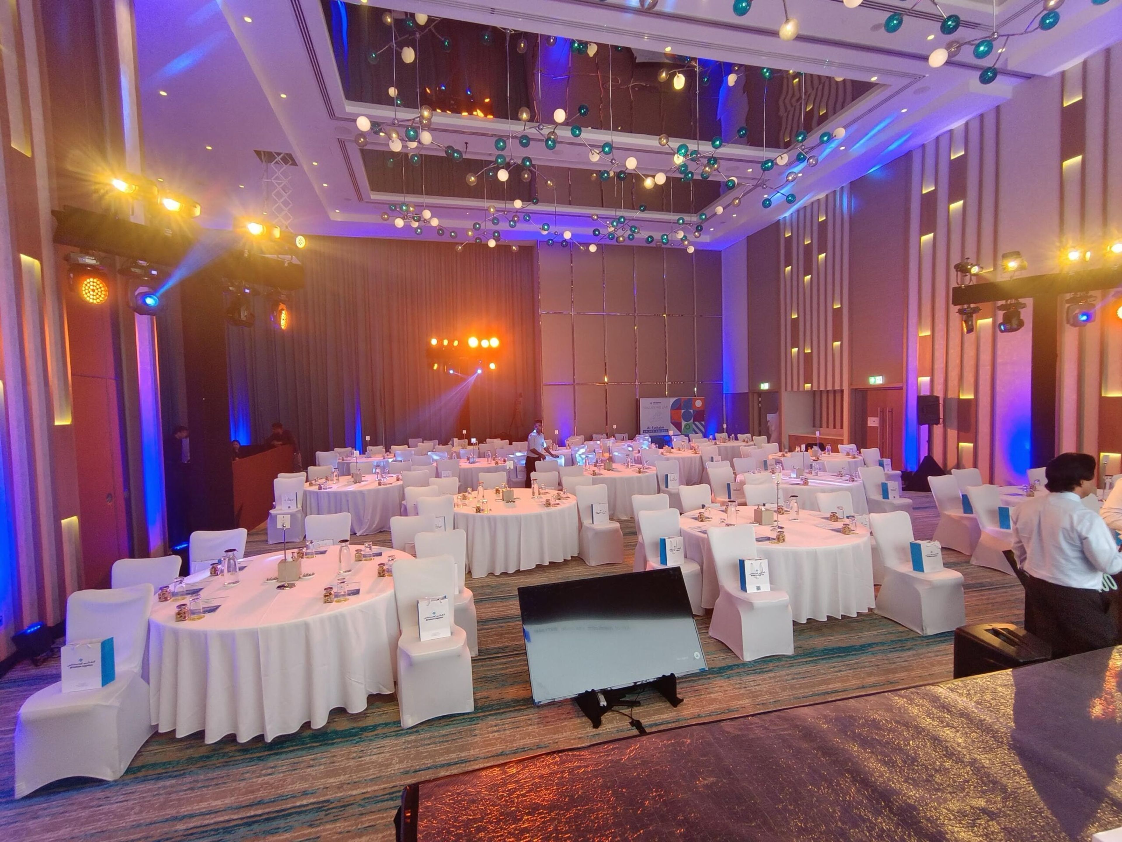 Banquet hall with white tables and chairs lit in blue and purple