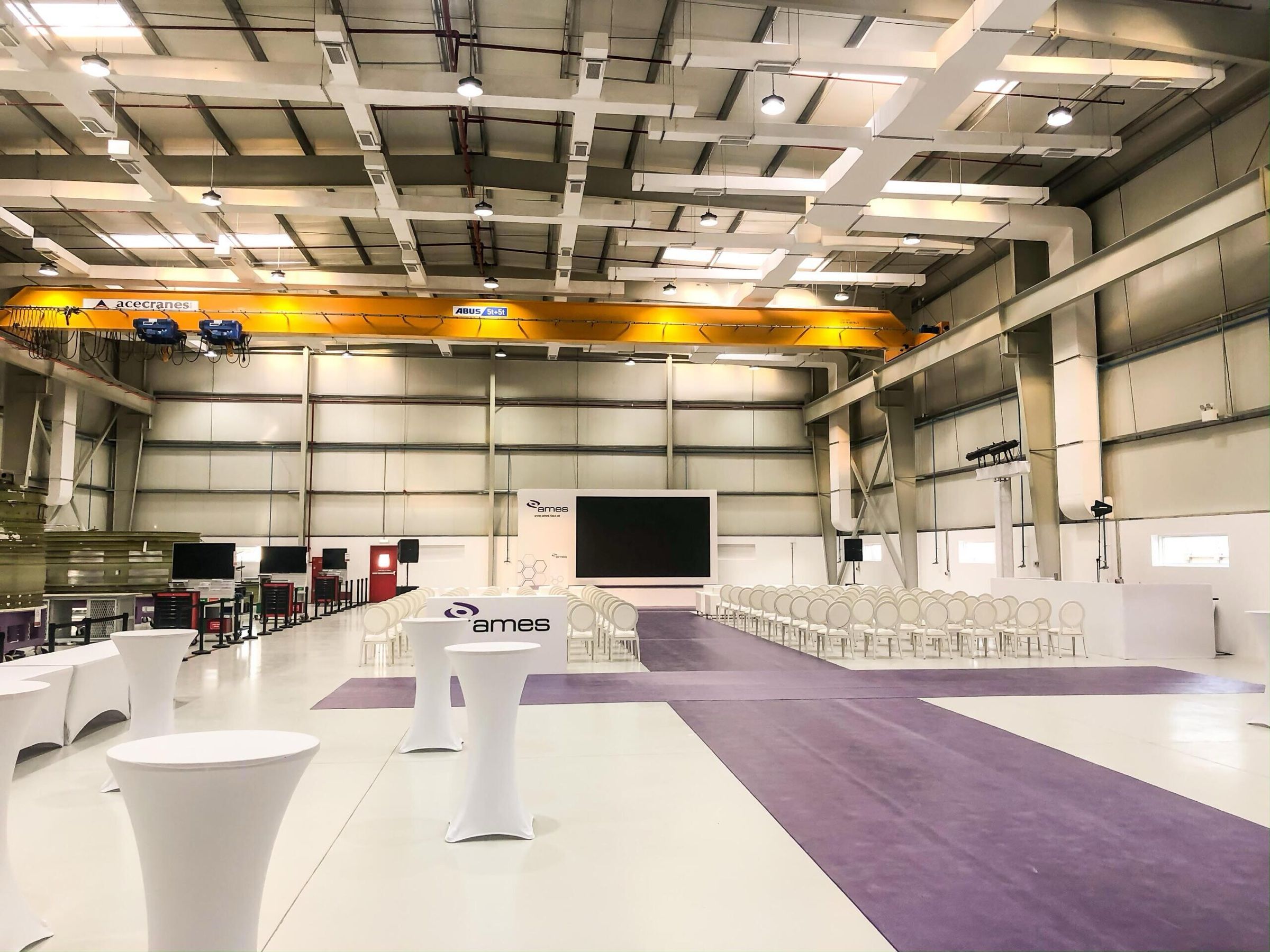 Large warehouse venue with white event furniture being set up for a corporate event