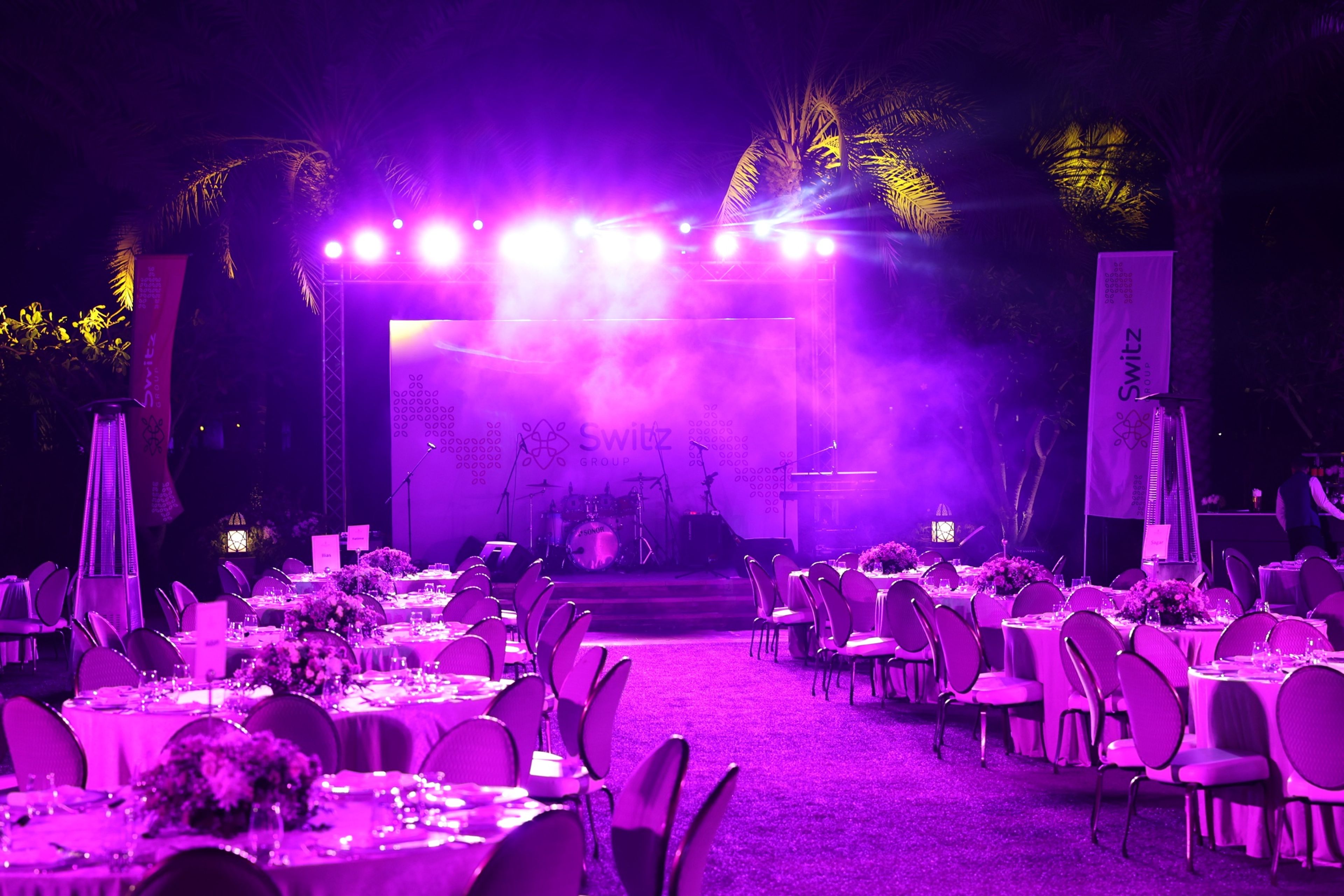 Outdoor evening event with purple stage lighting and lounge seating