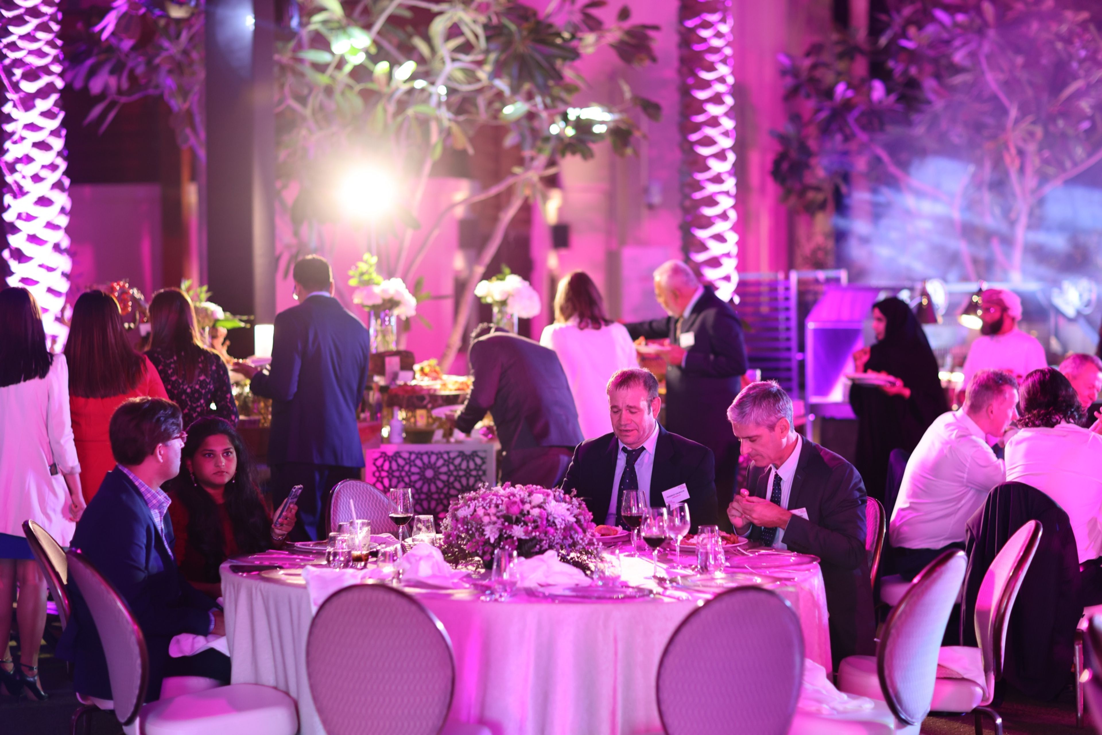 Guests at a gala dinner with pink lighting and floral décor
