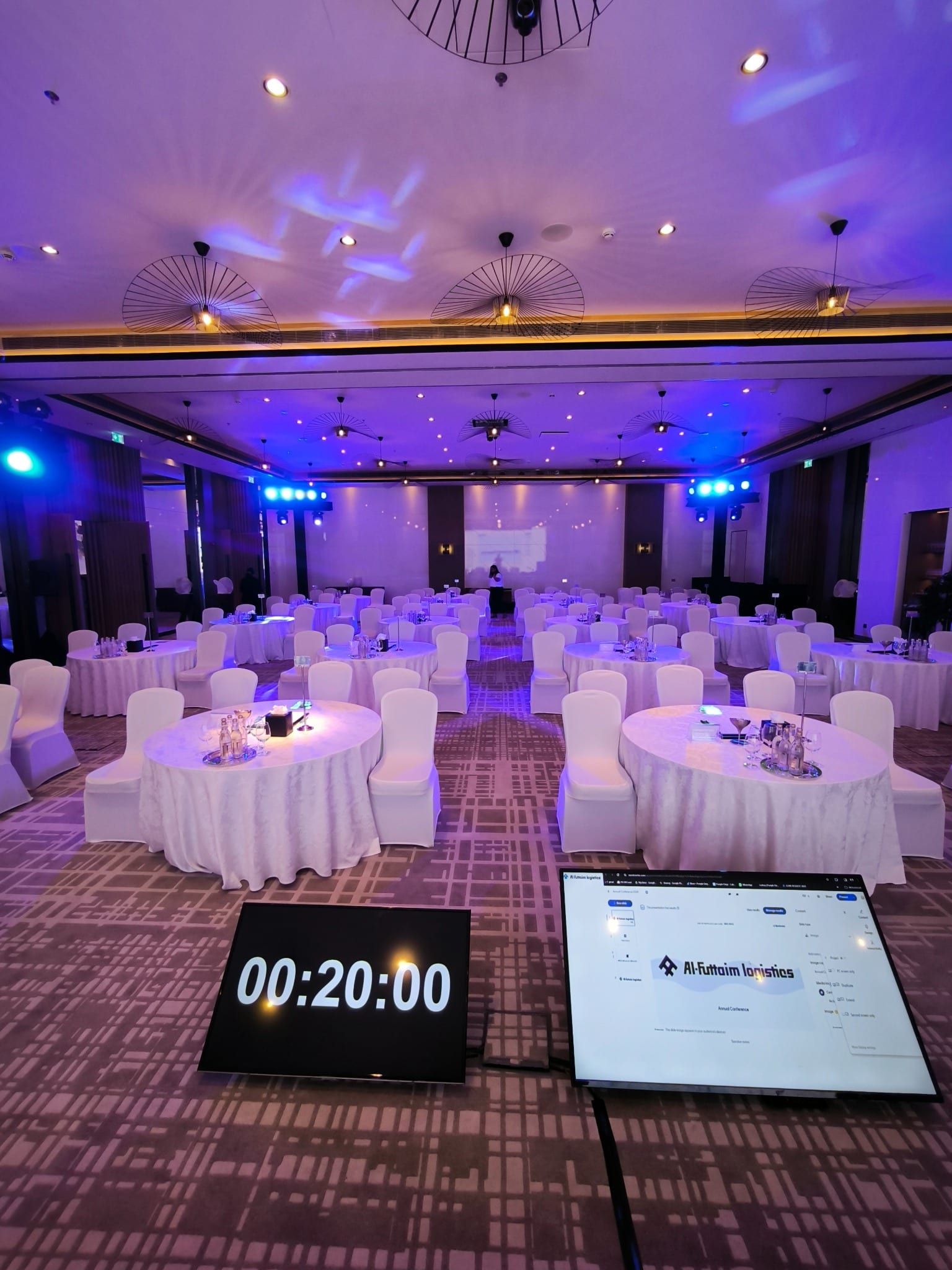 Ballroom set with round tables, blue uplighting and a stage countdown timer before the Al-Futtaim Logistics conference