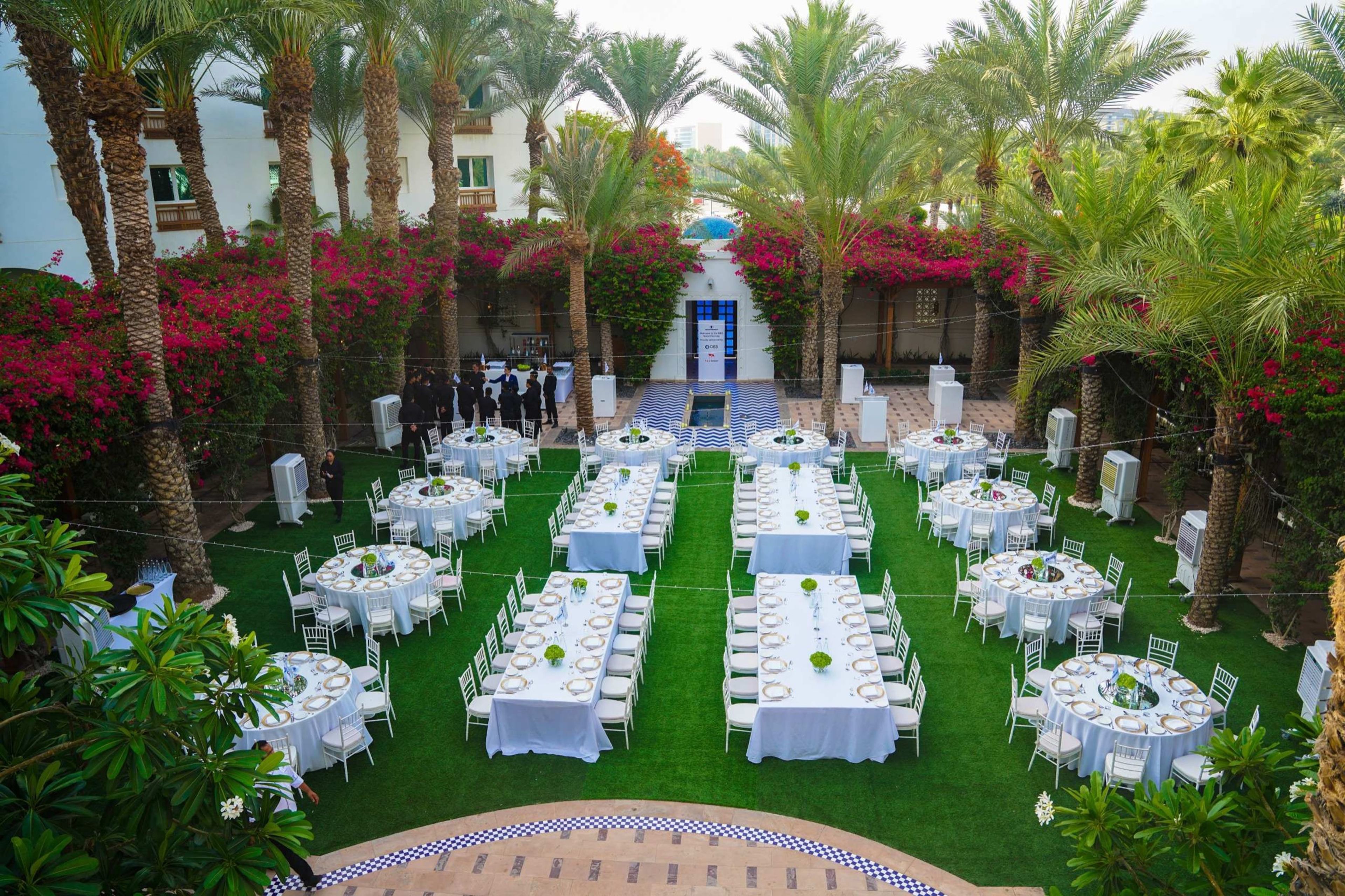 Garden gala dinner with long white tables among palm trees