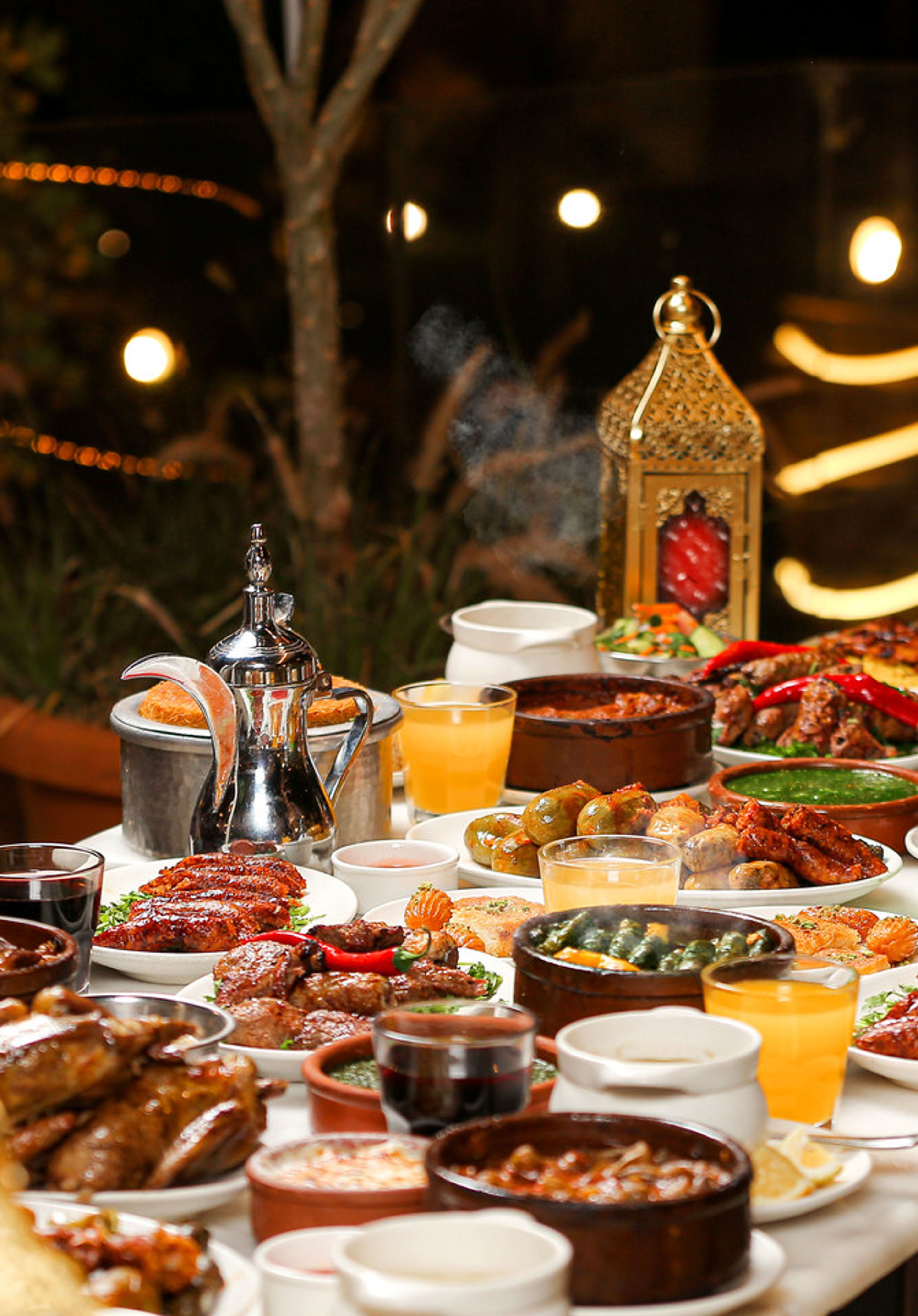 Iftar table with grilled meats, stuffed vegetables, juices, an Arabic coffee pot and a Ramadan lantern