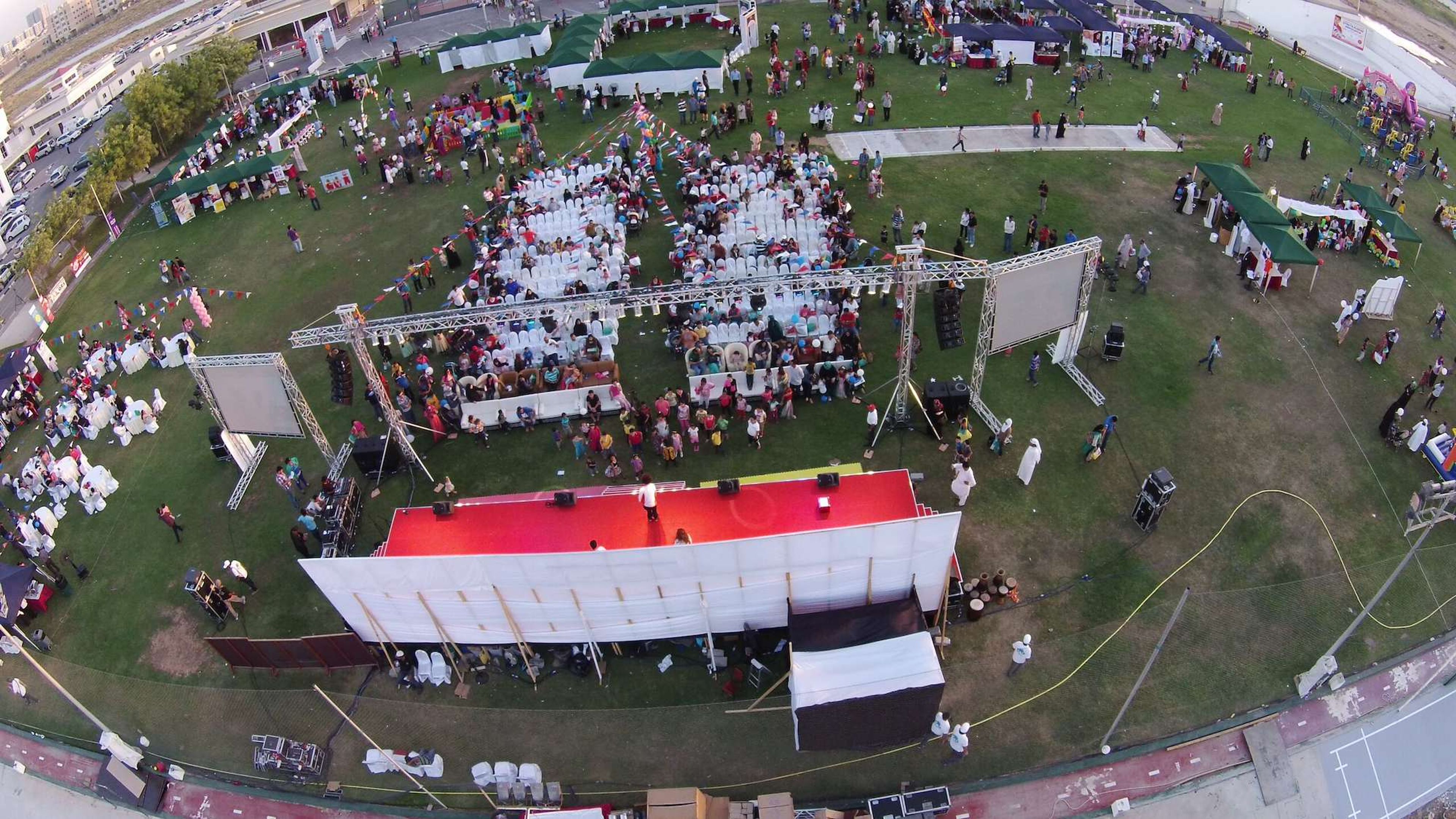 Aerial view of a corporate family day in the UAE with a main stage, LED screens, guest seating and activity stalls on open grass