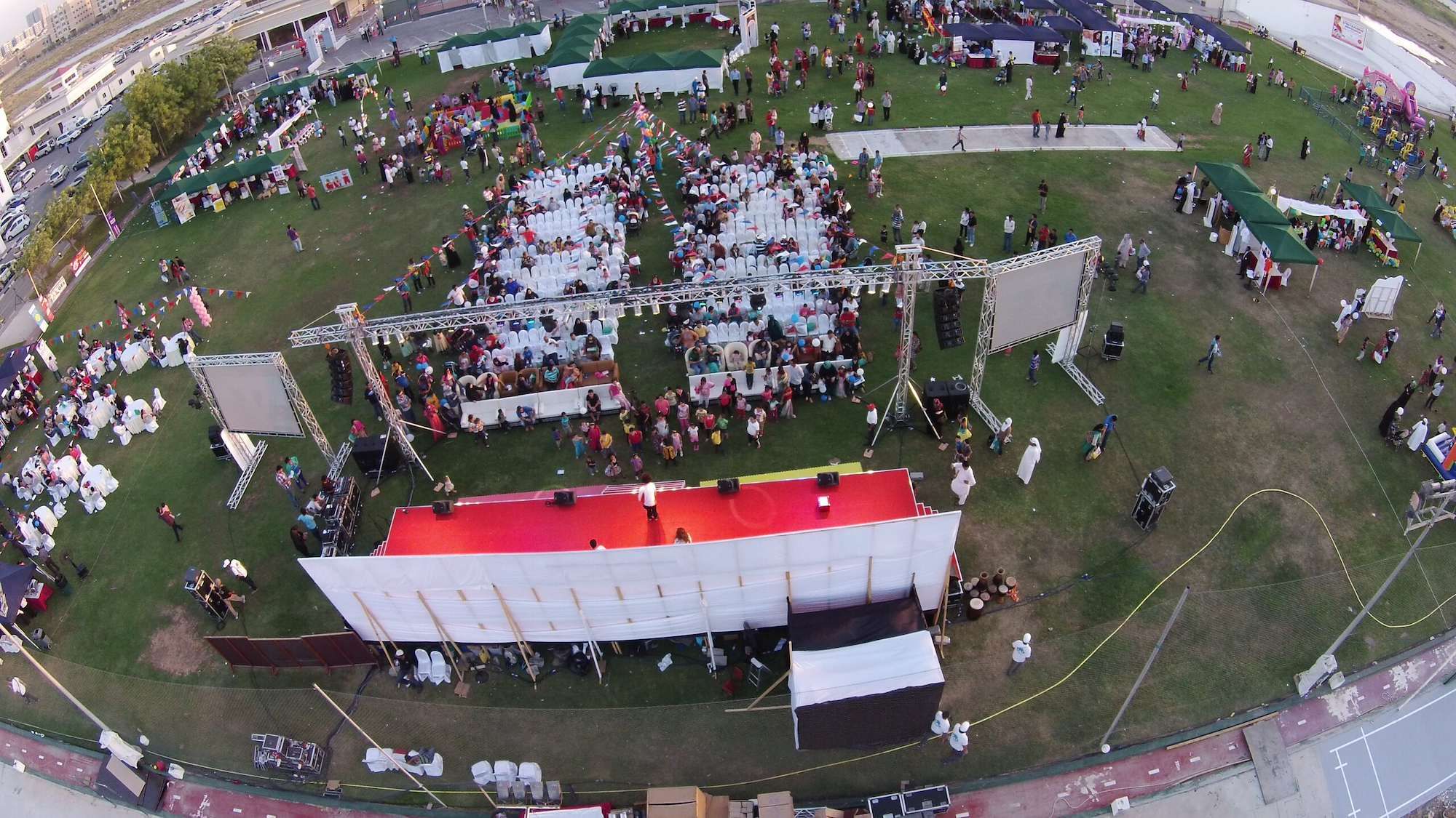 Aerial view of a corporate family day in the UAE with a main stage, LED screens, guest seating and activity stalls on open grass
