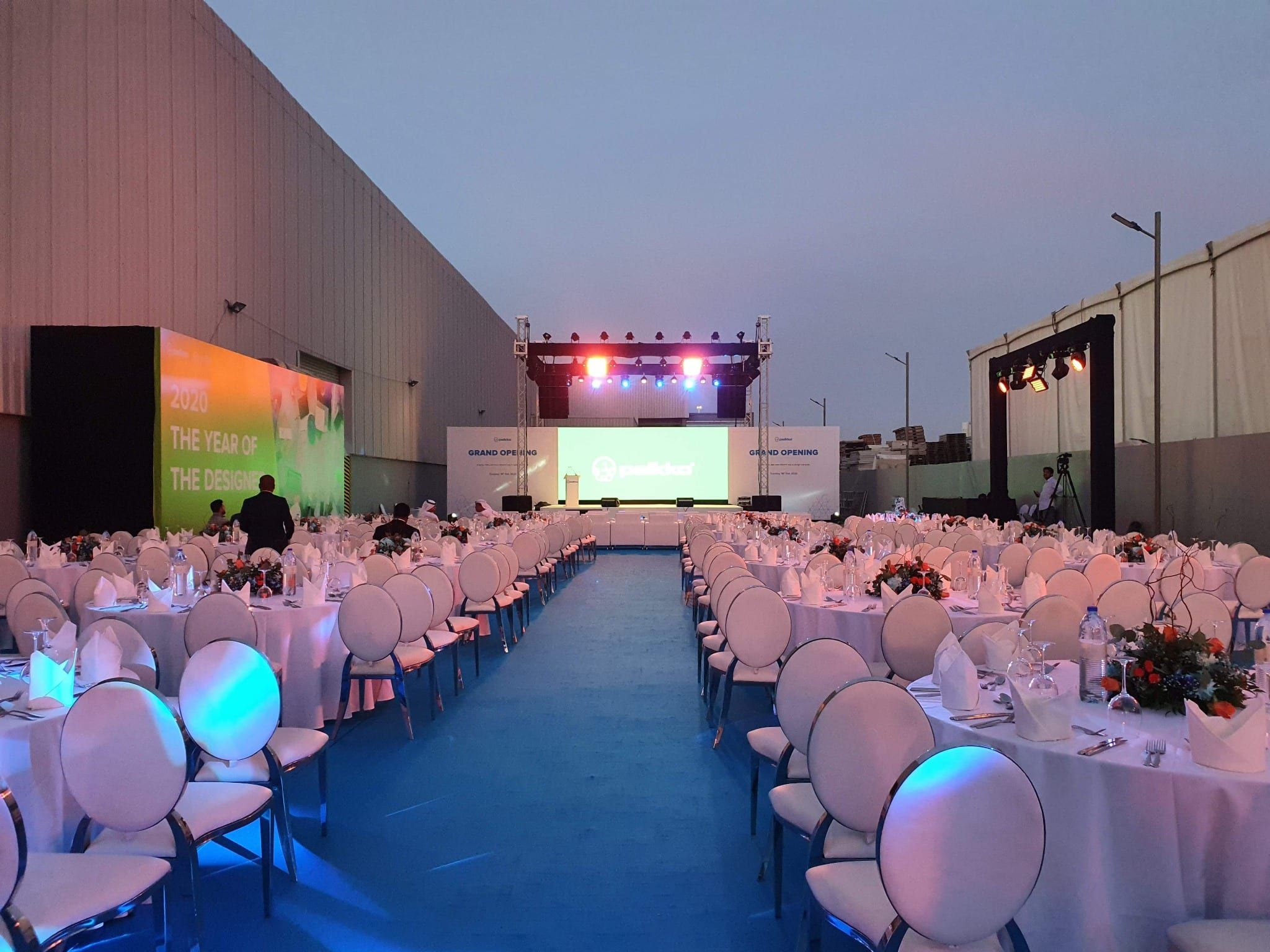 Dinner tables along a blue carpet aisle leading to the stage outside the Peikko facility