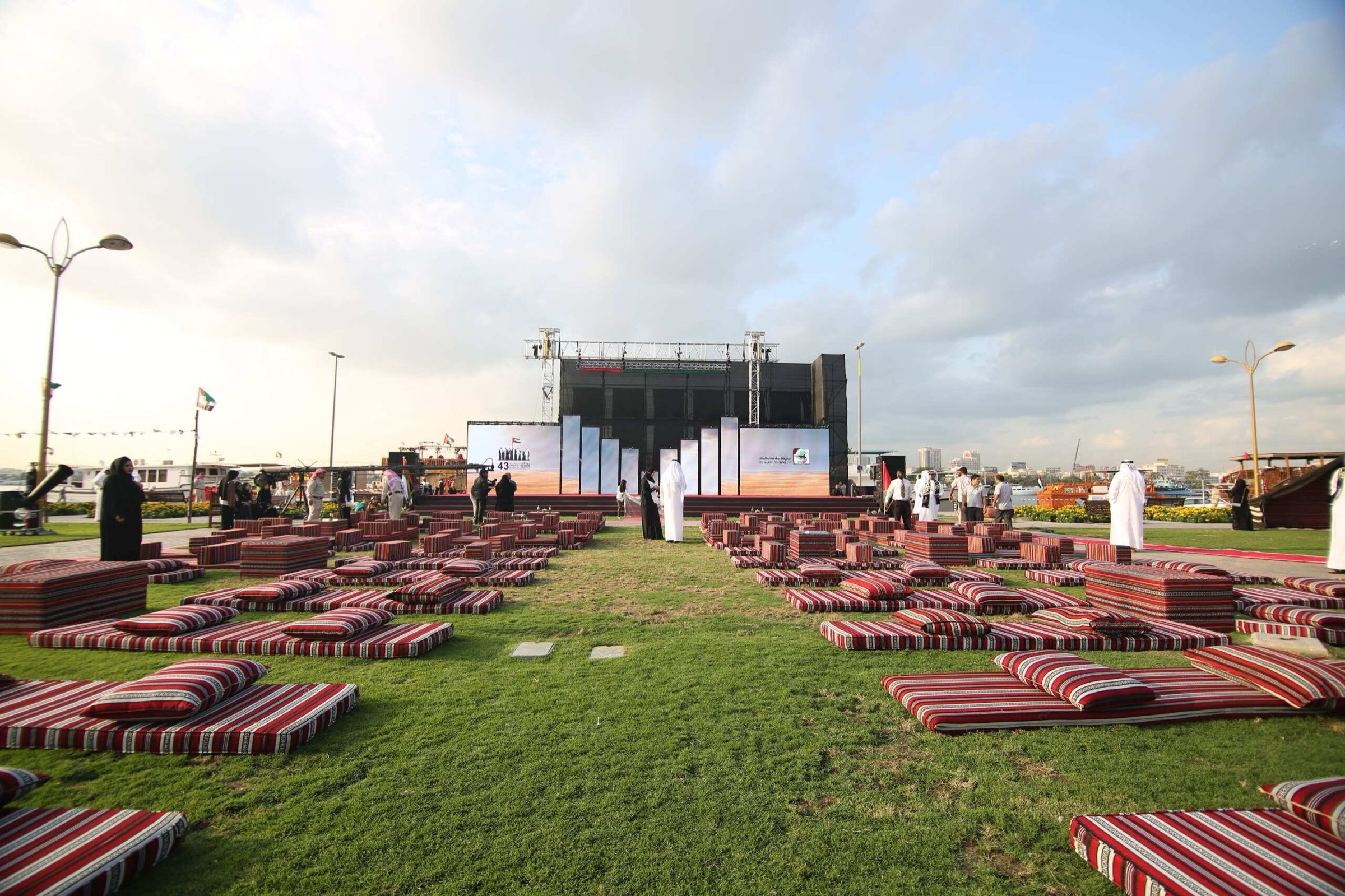 Outdoor majlis seating with carpets and cushions arranged on a lawn at sunset