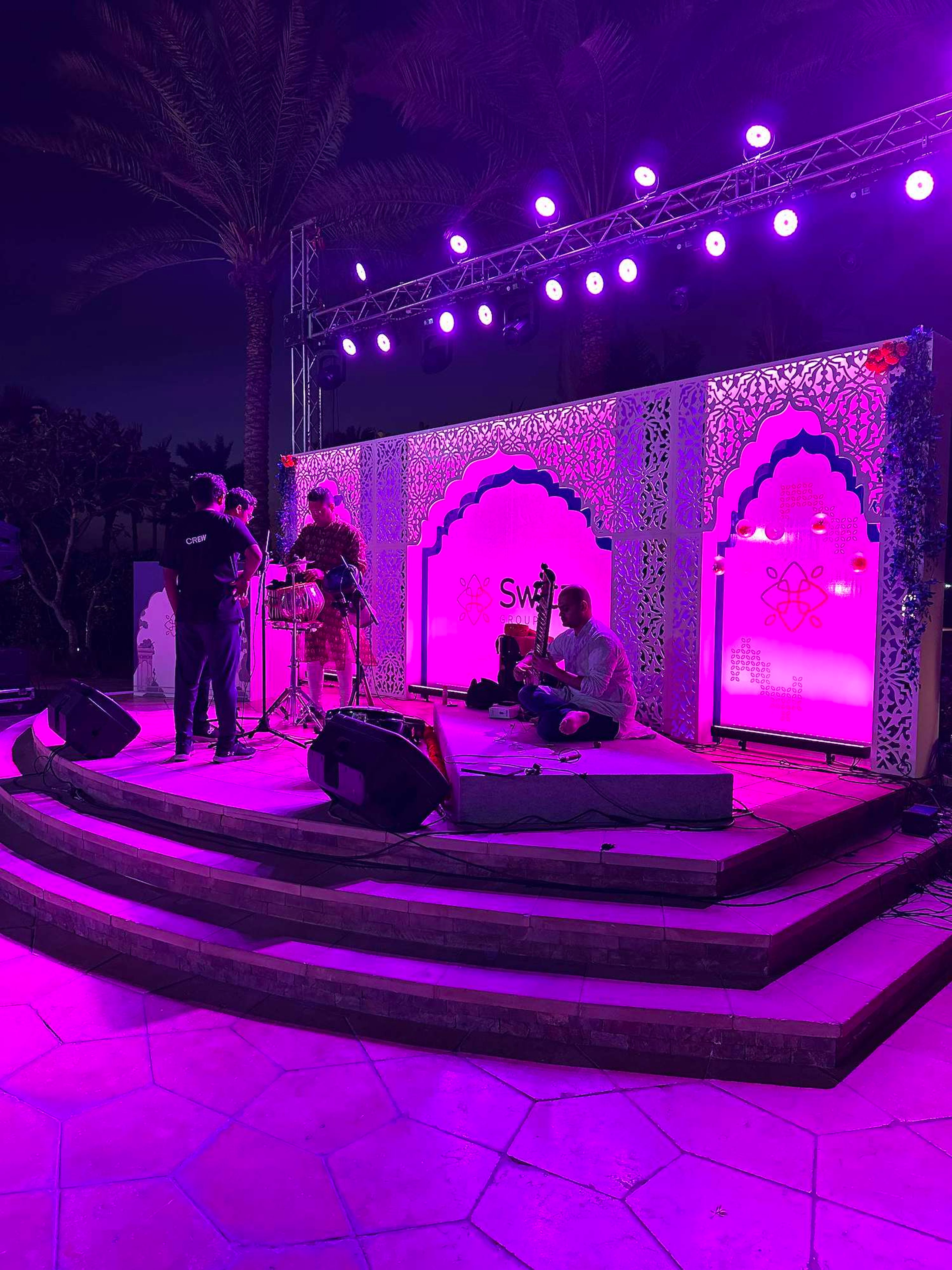Outdoor corporate evening stage in Dubai with truss lighting, carved backdrop panels and live musicians setting up