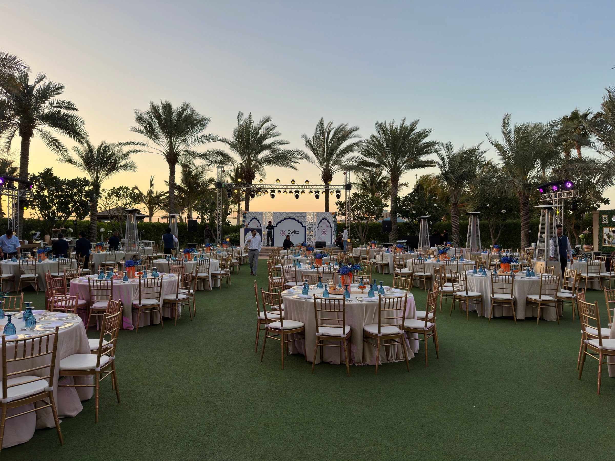 Outdoor dinner with round tables set on a lawn among palm trees
