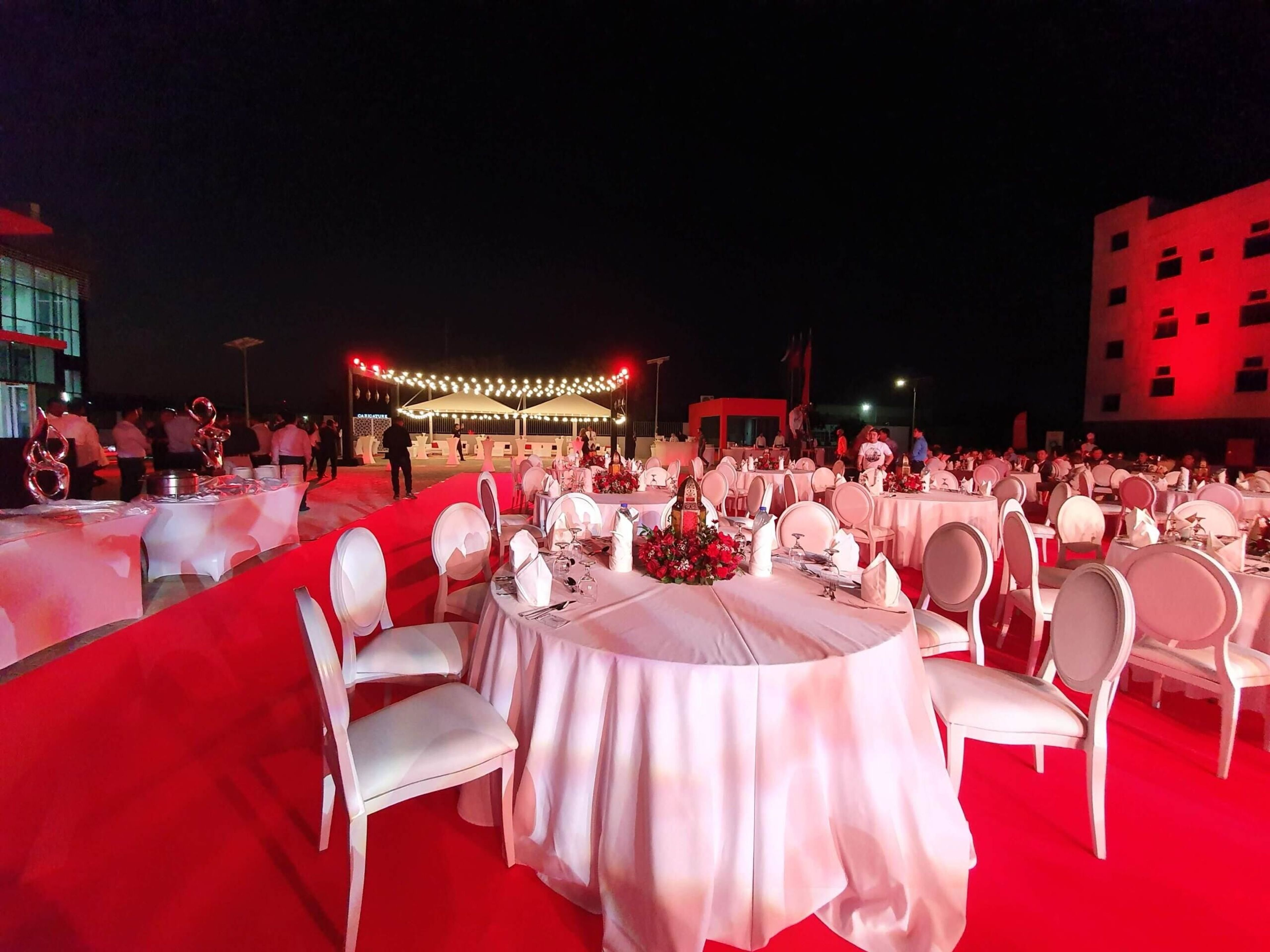 Night-time outdoor dinner with round tables on a red carpet