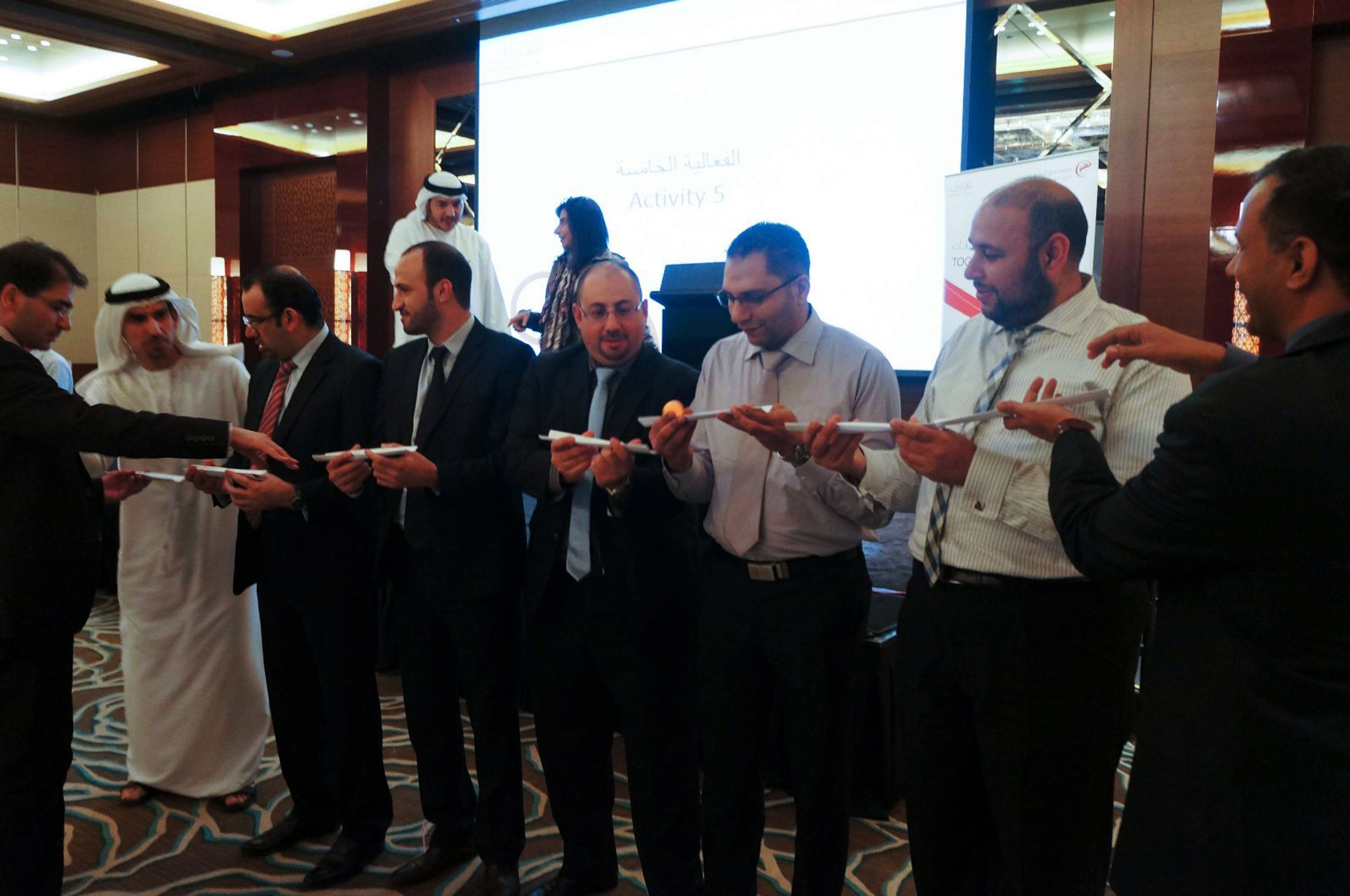 Colleagues passing a ball along a line of half-pipes during an indoor team building activity in a hotel function room