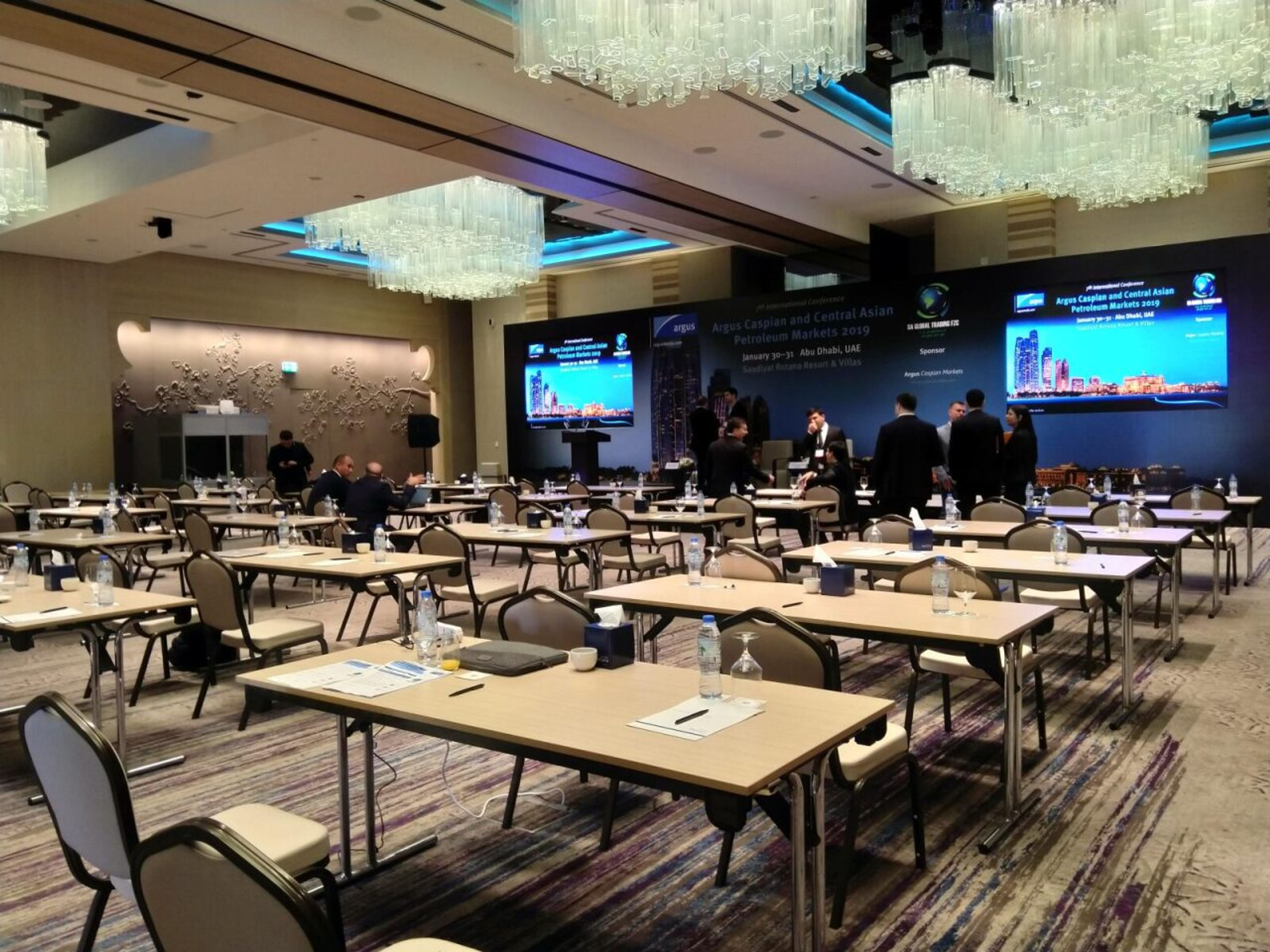 Hotel ballroom set with classroom-style tables and stage screens for a conference