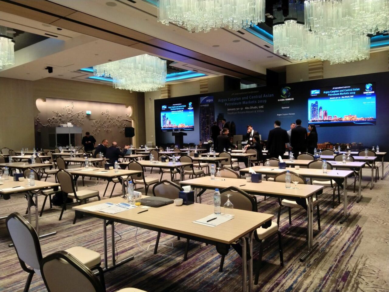 Hotel ballroom set with classroom-style tables and stage screens for a conference