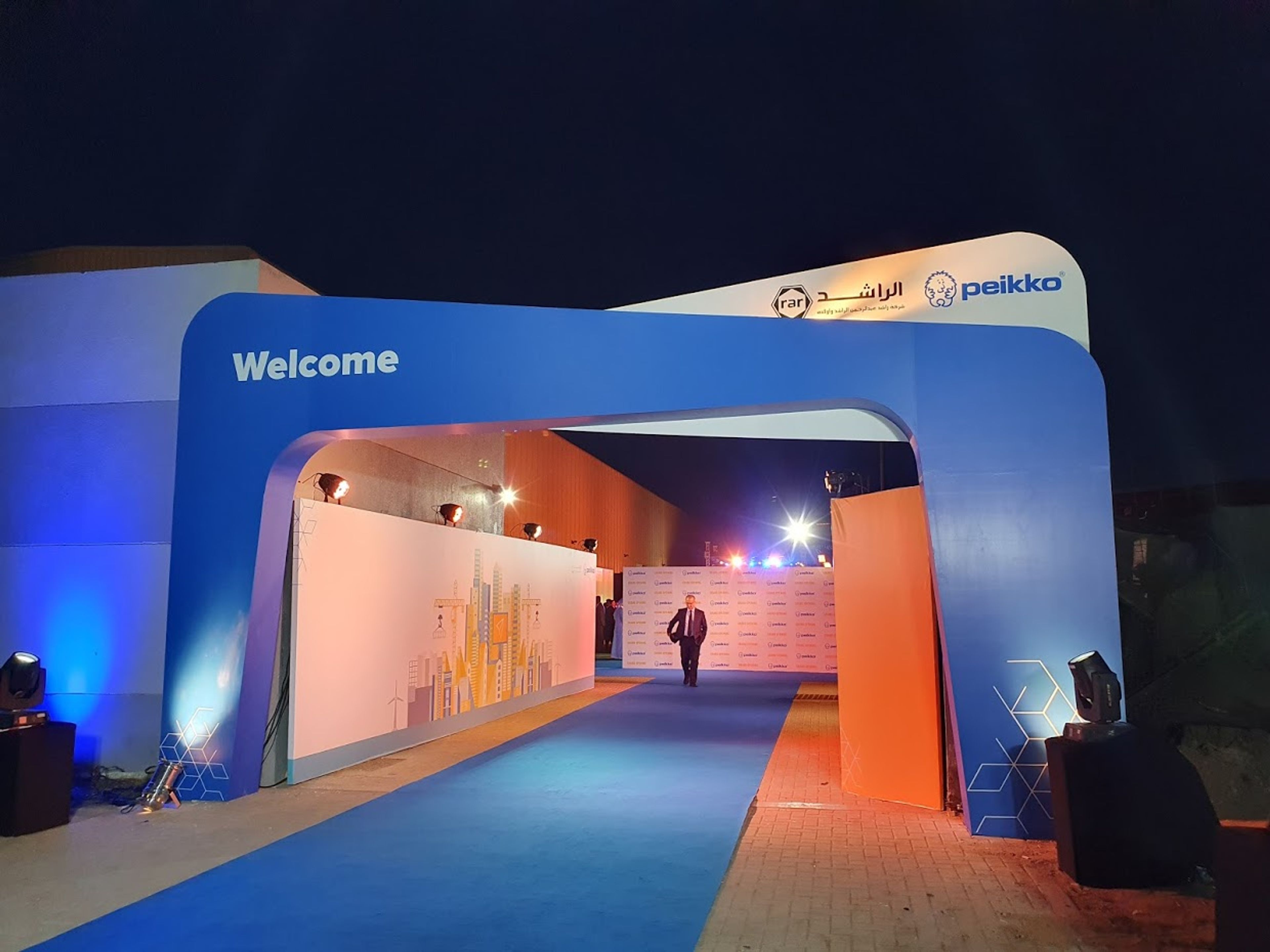 Illuminated Peikko-branded welcome arch and blue carpet leading guests into a facility grand opening at night