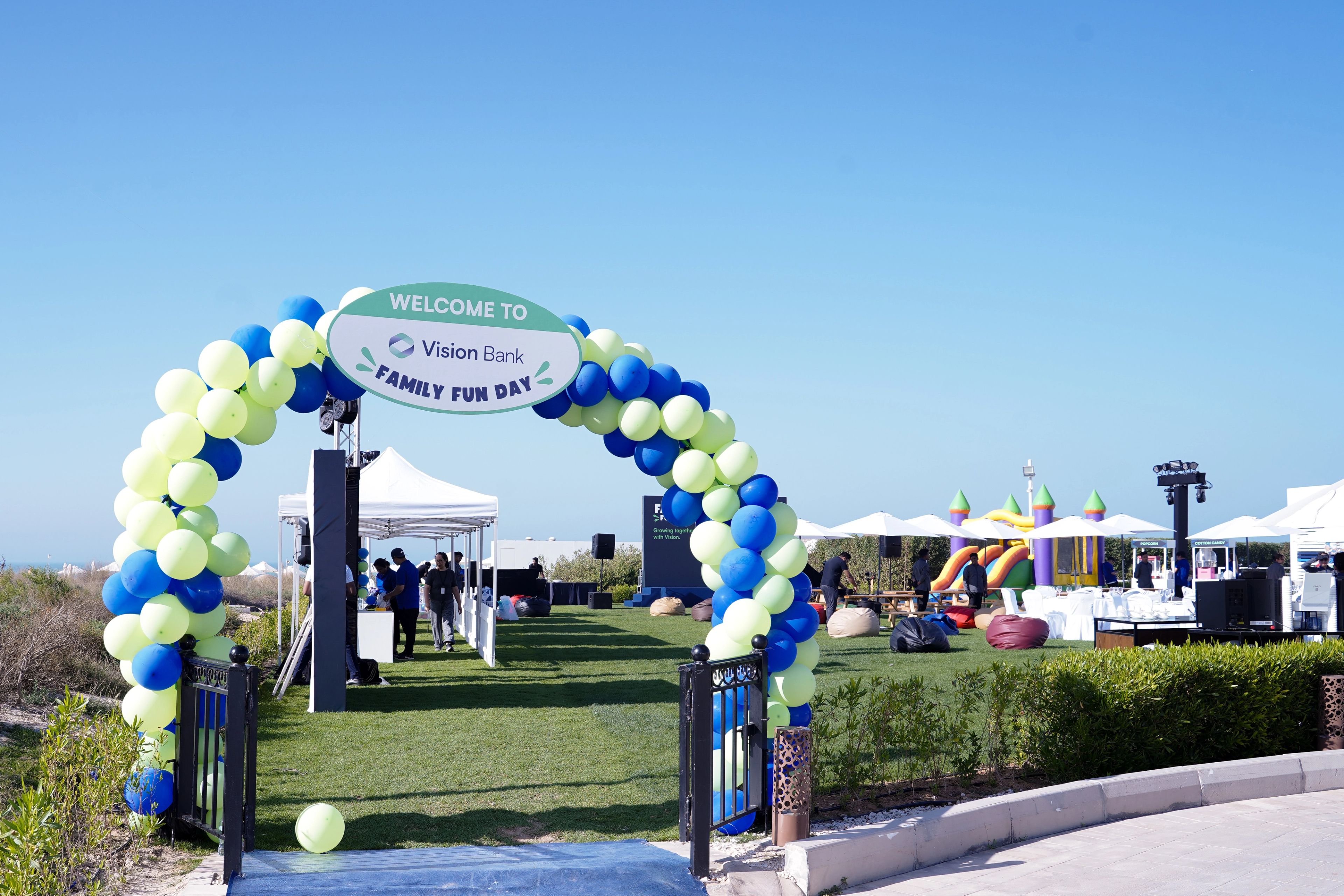 Aerial view of a corporate family day in the UAE with a main stage, LED screens, guest seating and activity stalls on open grass