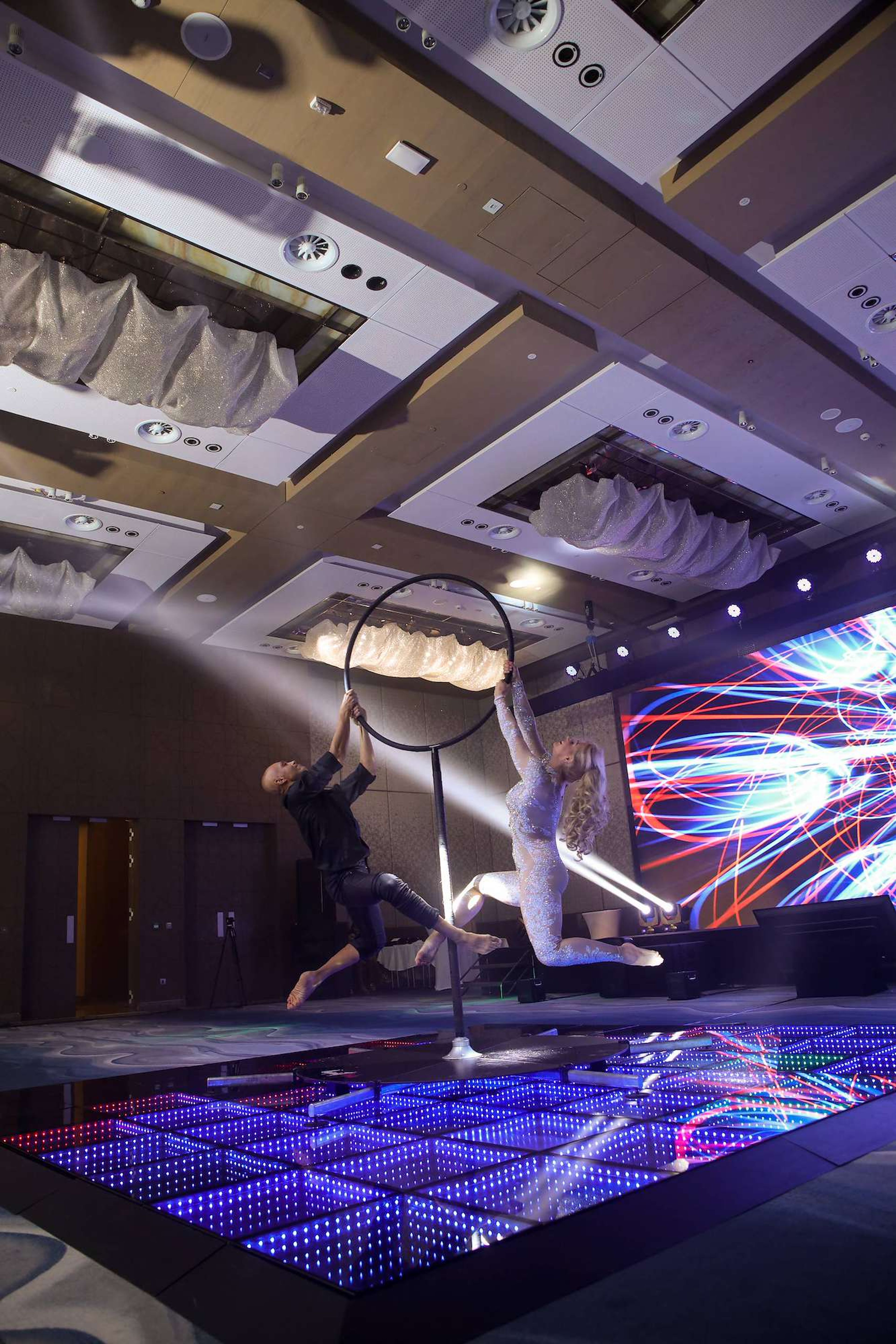 Aerial hoop act above an LED dance floor in a hotel ballroom with moving head lights and an LED wall