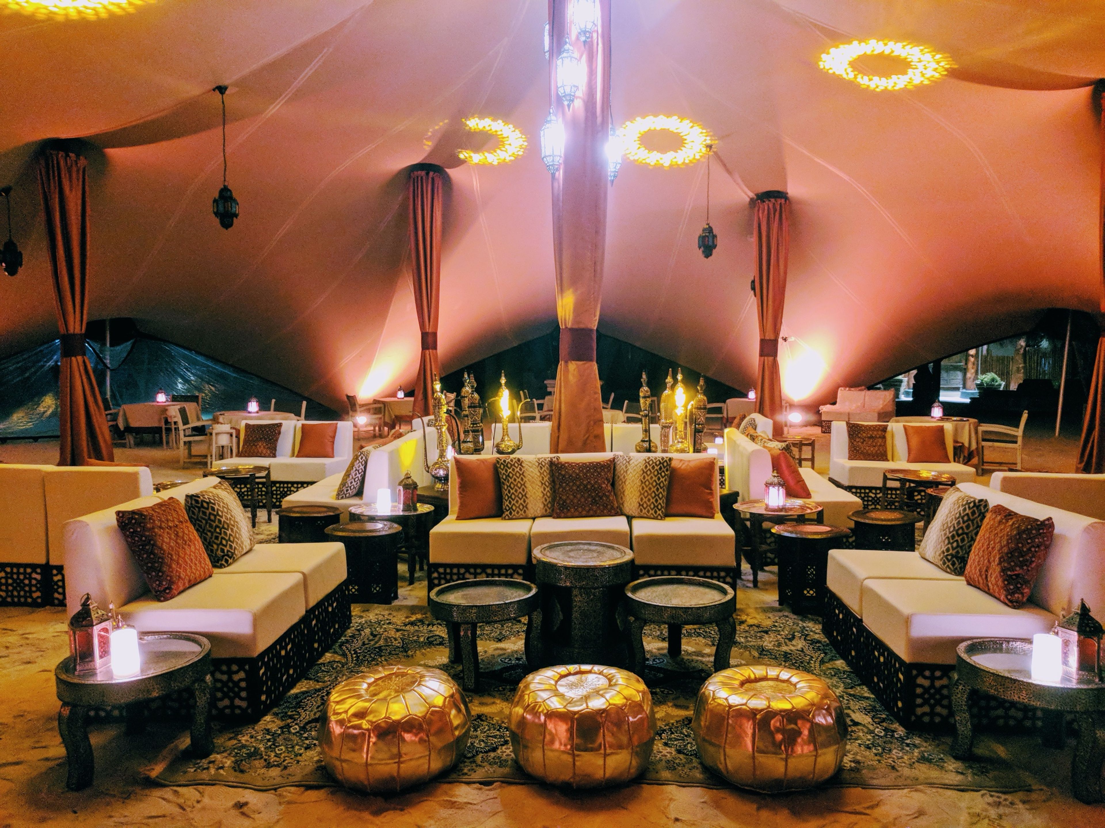 Tented Ramadan lounge with cream sofas, patterned cushions, gold leather poufs, lanterns and warm evening lighting