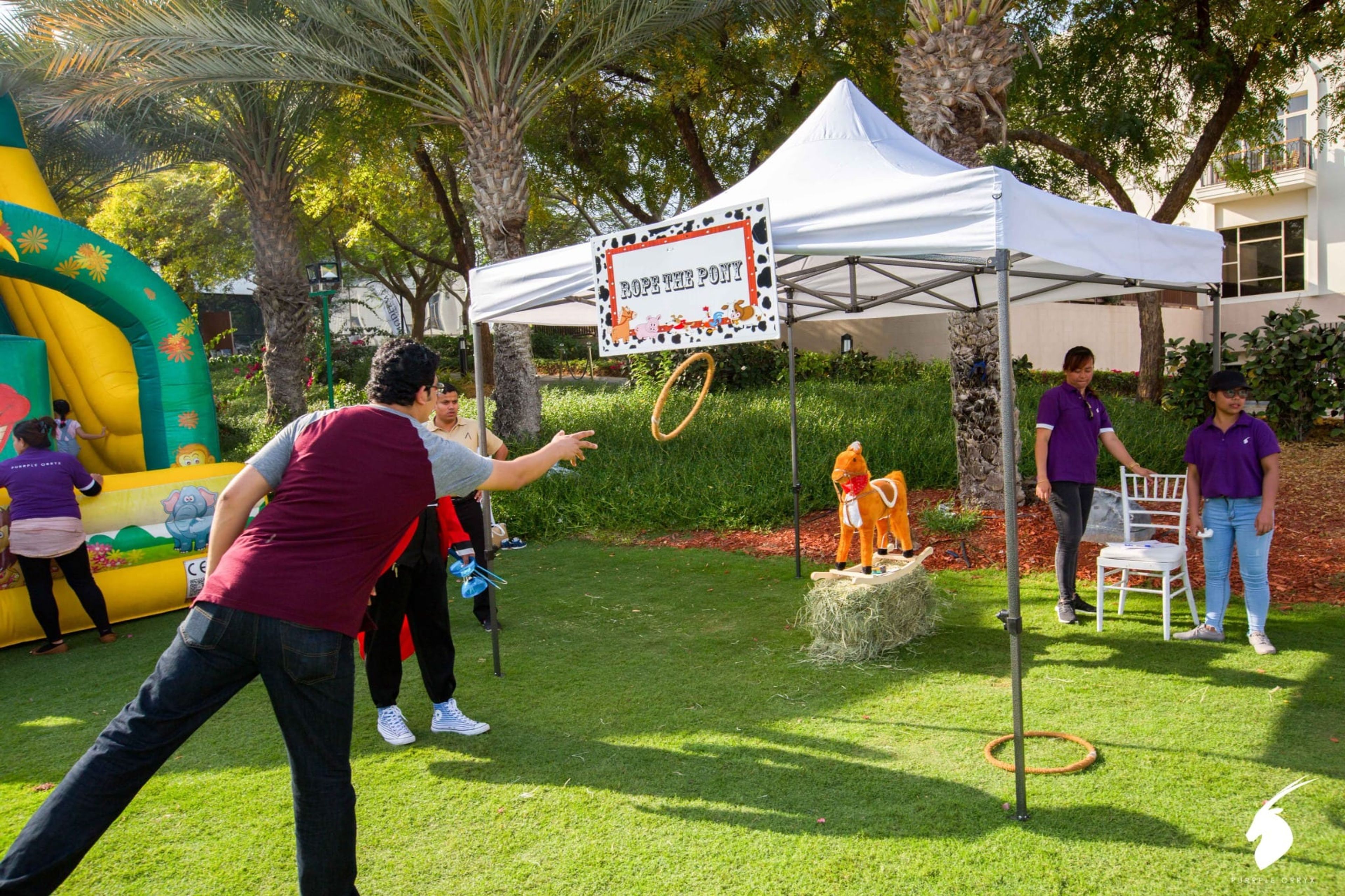 Guests playing a ring toss carnival game under a white gazebo