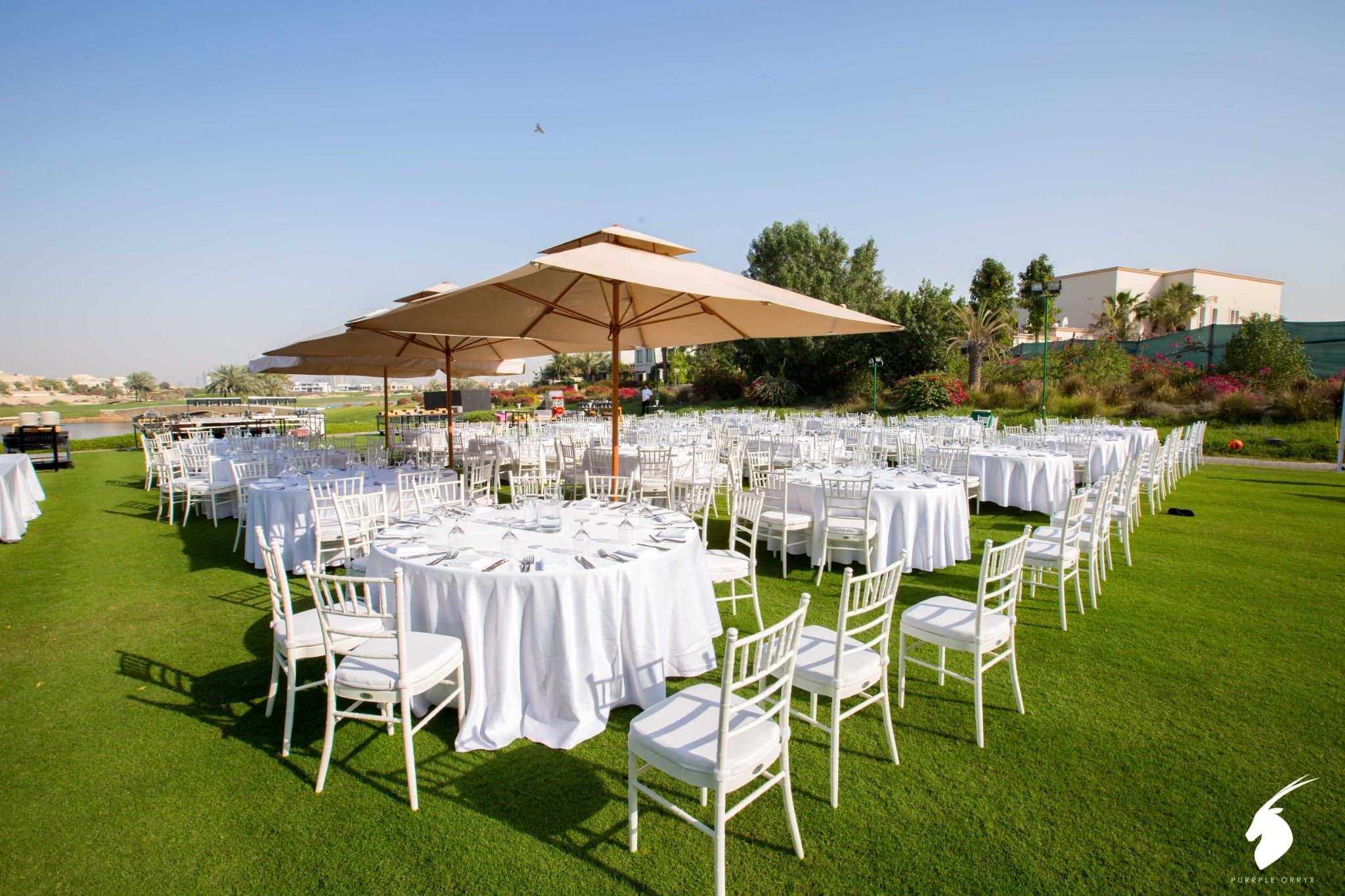 Round dining tables with white linen and garden umbrellas on the lawn at Address Montgomerie