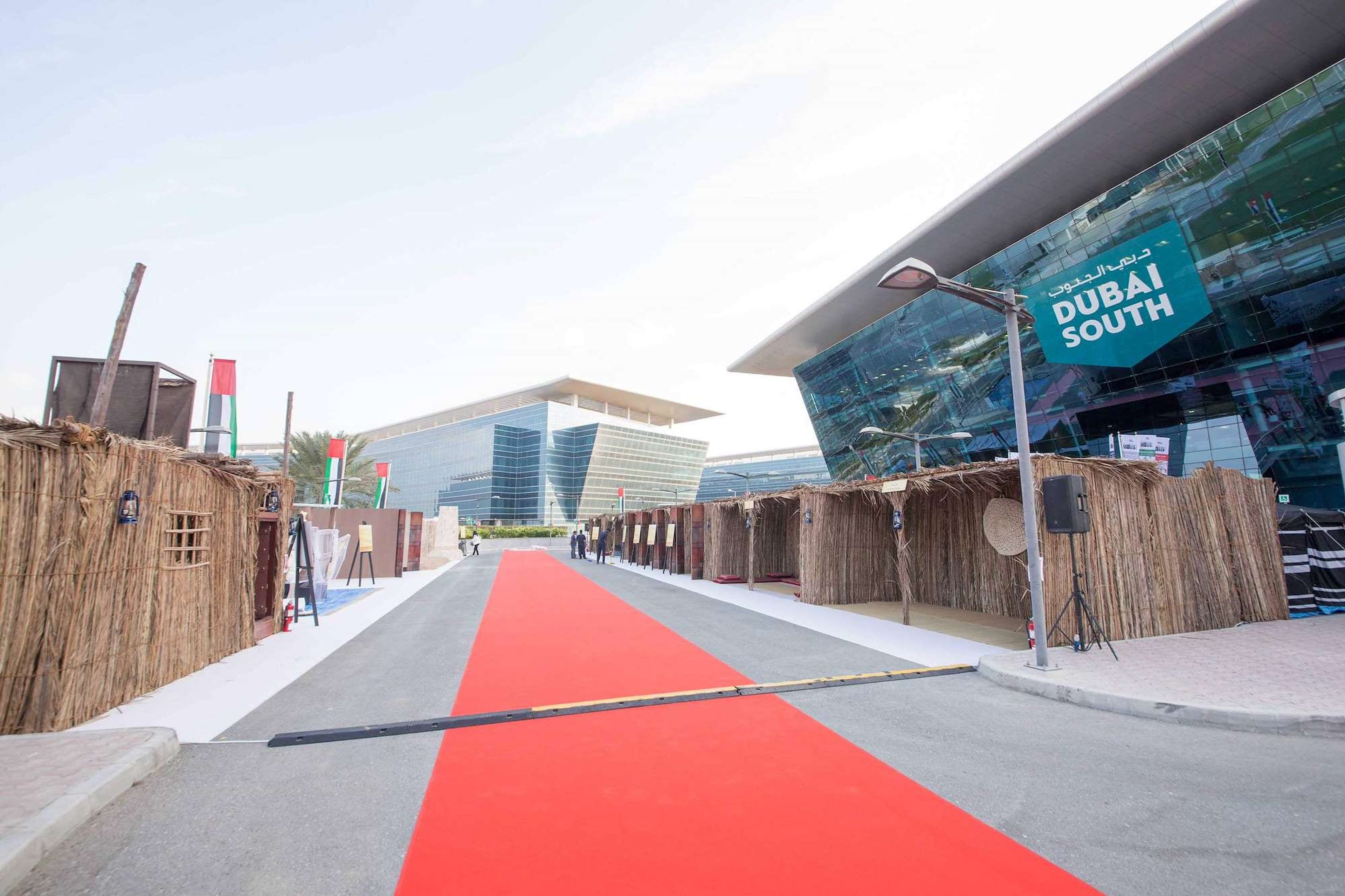 Red carpet heritage street with palm frond souq stalls and UAE flags outside a Dubai free zone headquarters for UAE National Day