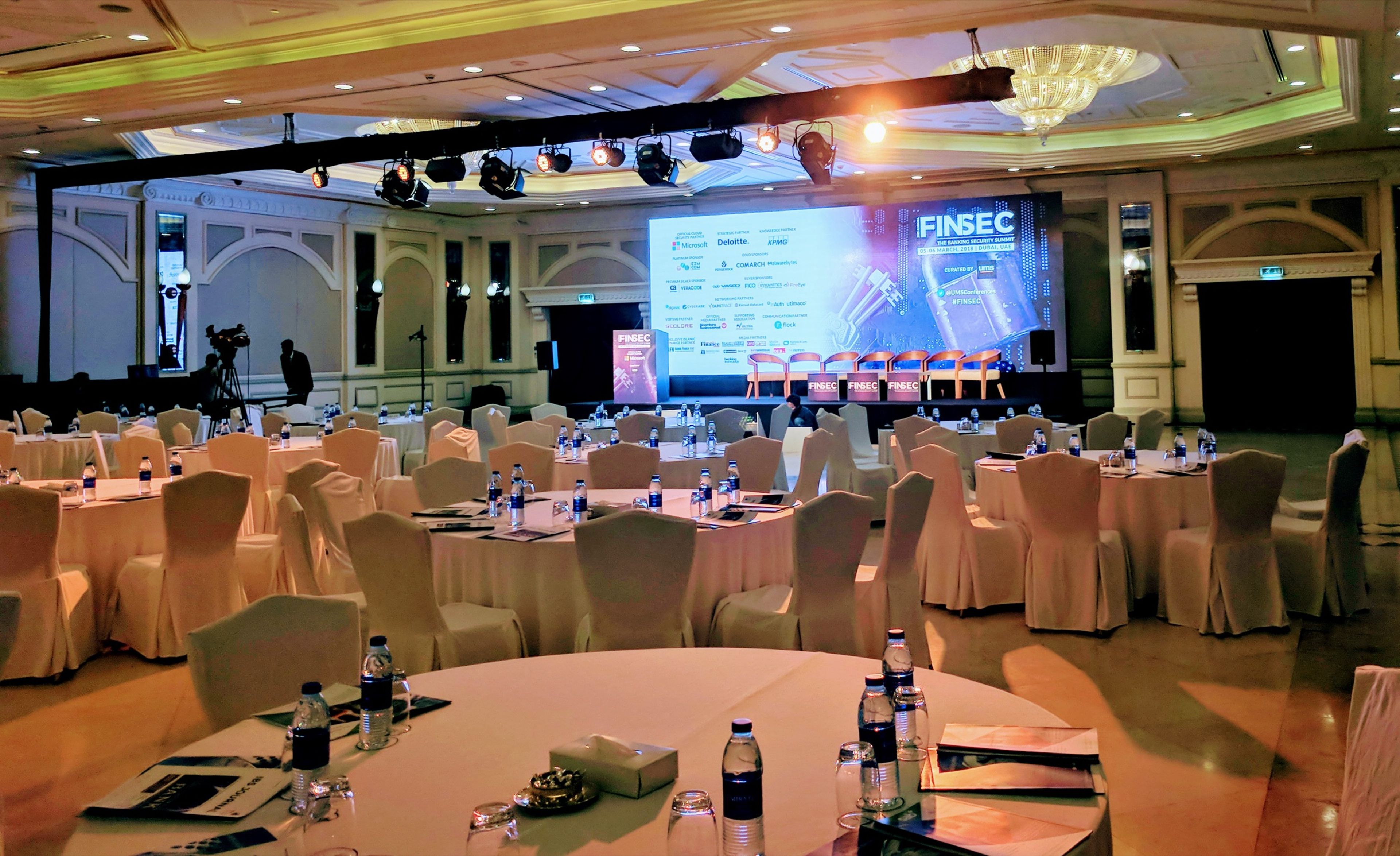 Ballroom set with round tables facing a stage screen for a conference