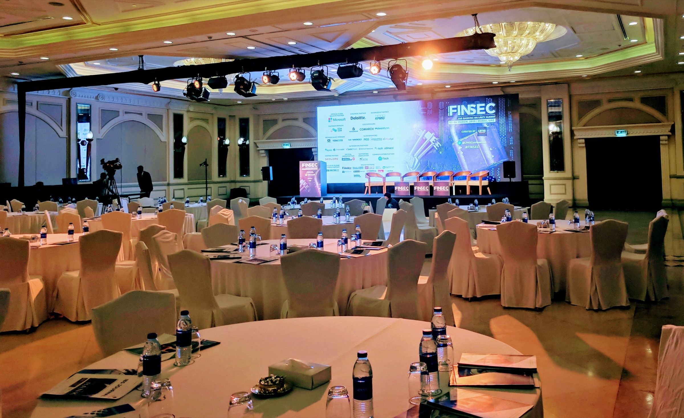 Ballroom set with round tables facing a stage screen for a conference